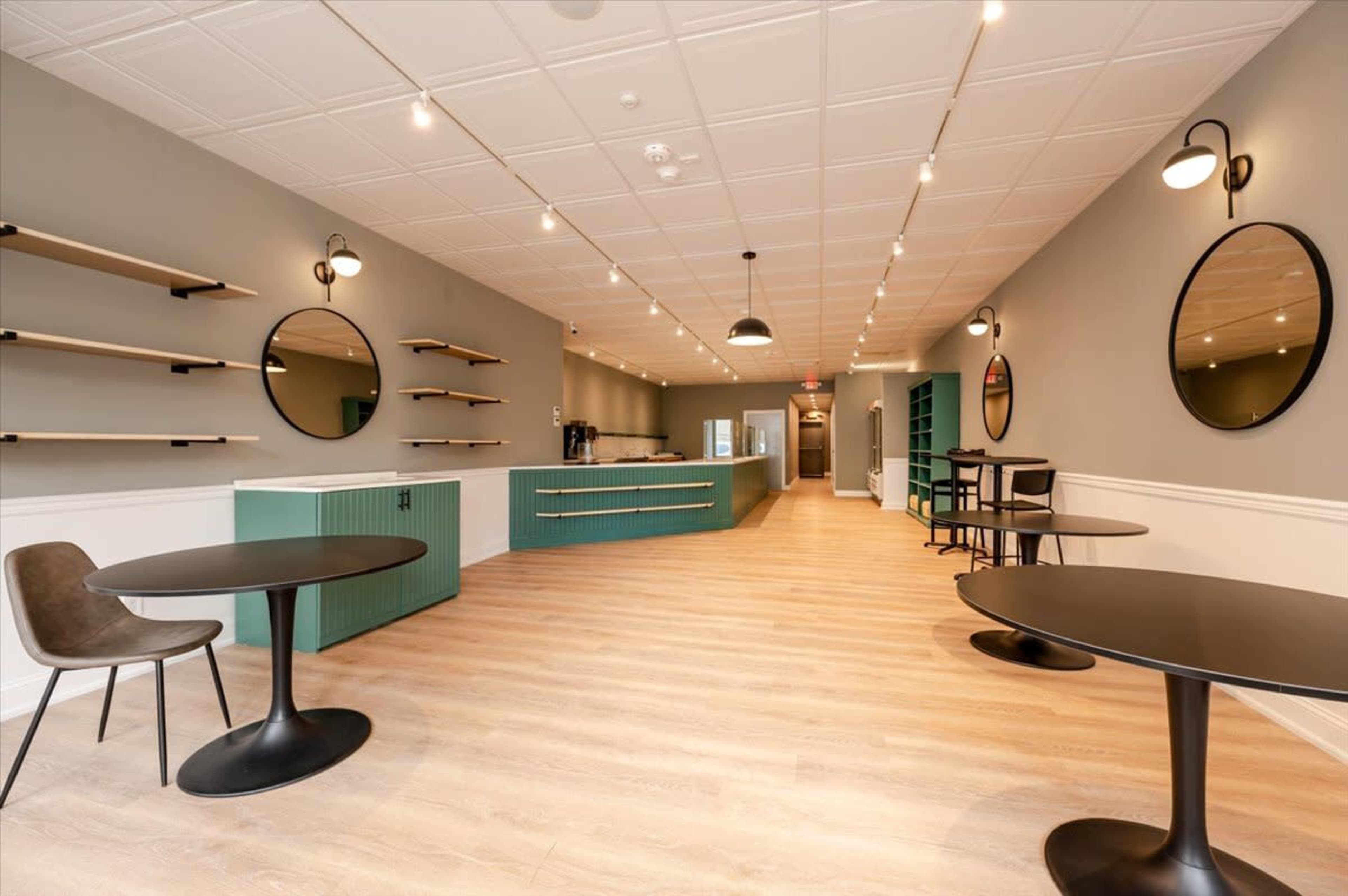 A modern, minimalist cafe interior with circular mirrors and green accents, featuring tables and open shelving along the walls.