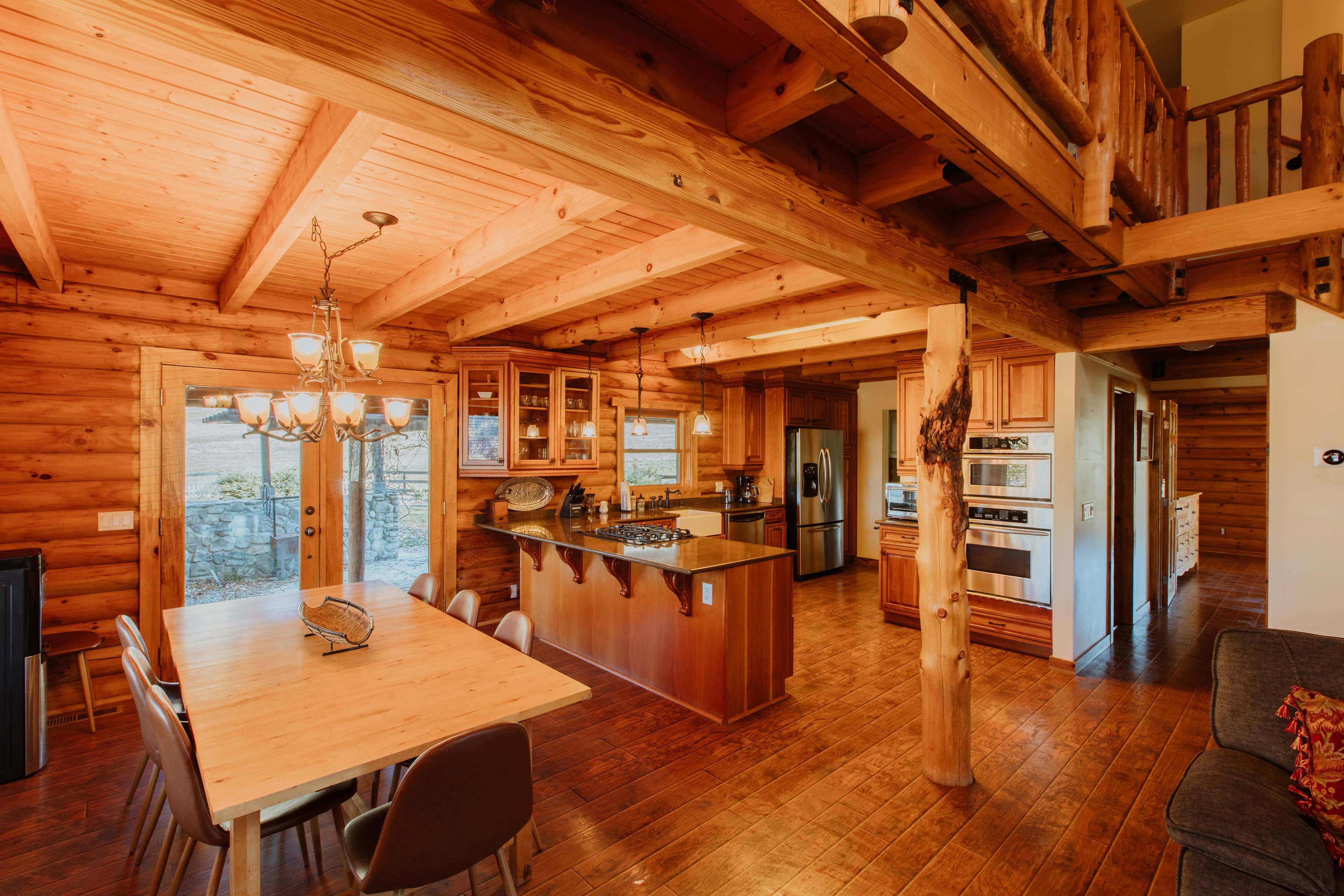 A spacious wooden kitchen and dining area with a large table, open layout, and a staircase leading to a loft.