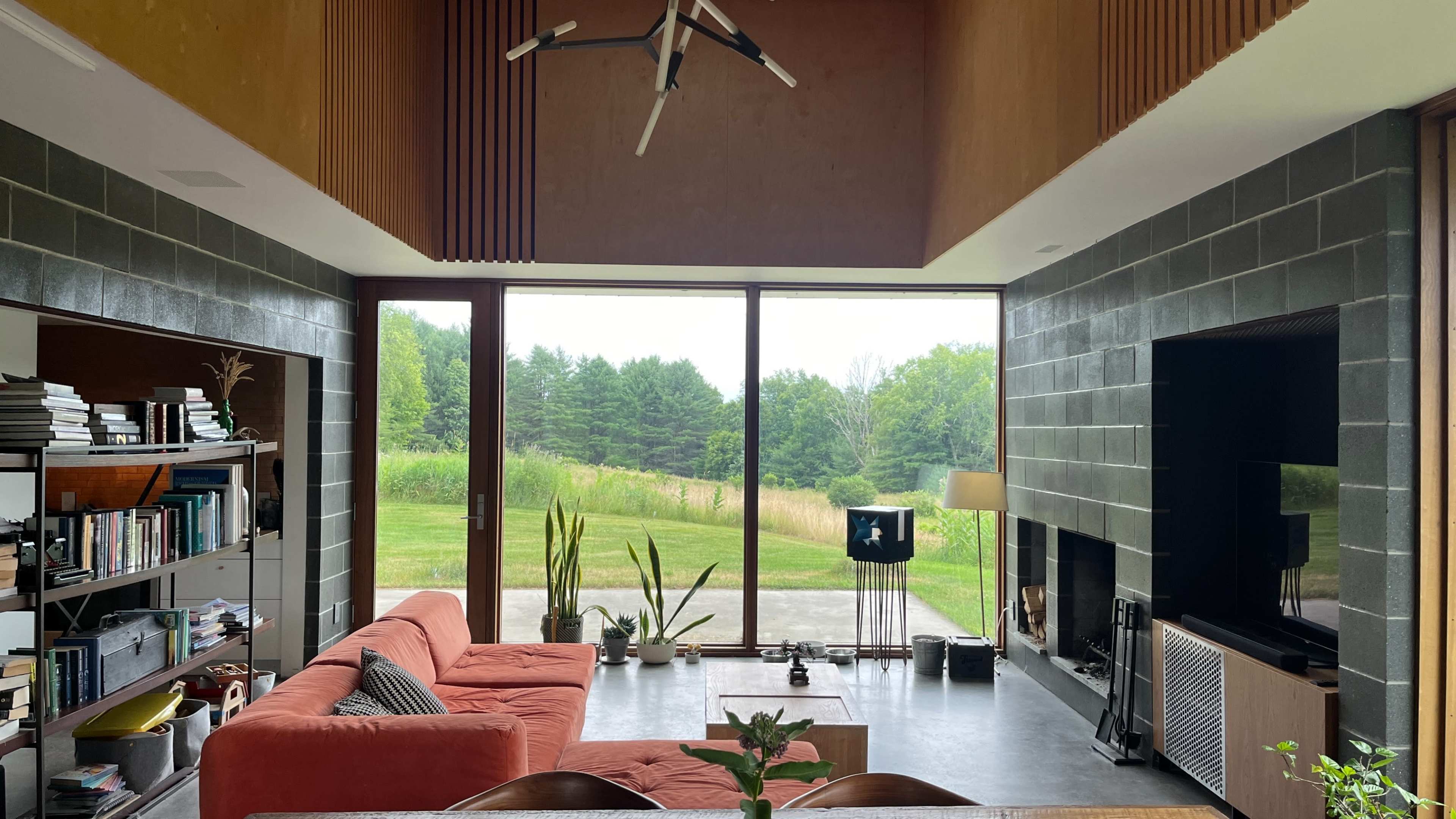 A spacious living room features a large window overlooking a green landscape, with a central sofa and modern furnishings.