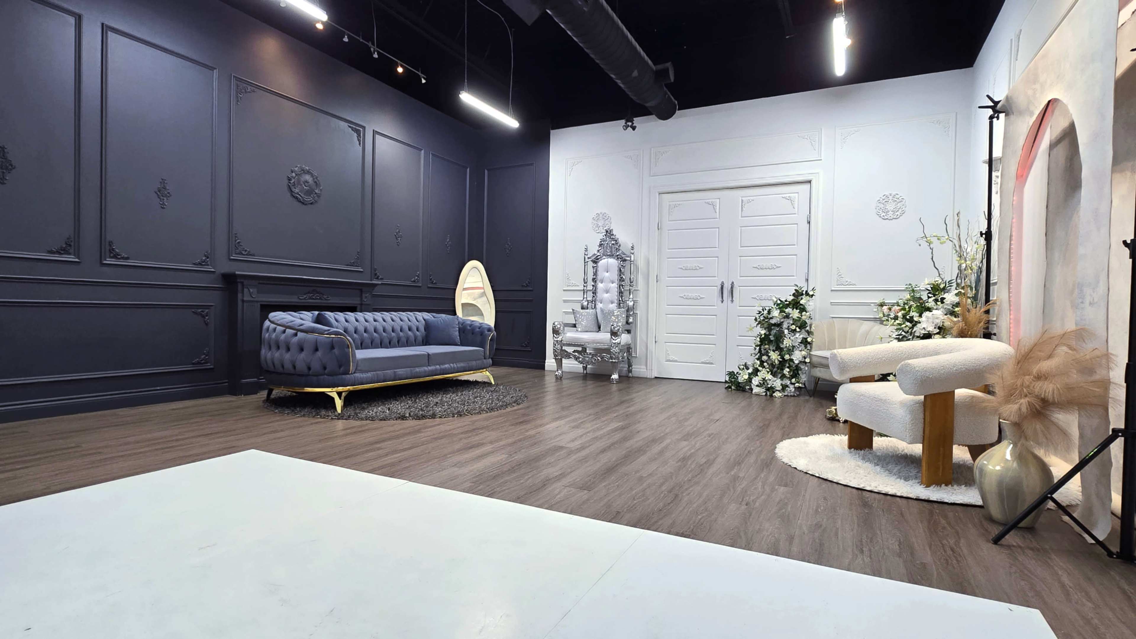 The image depicts a stylish studio interior featuring a blue sofa, a white throne-like chair, and decorative elements against dark and light walls.