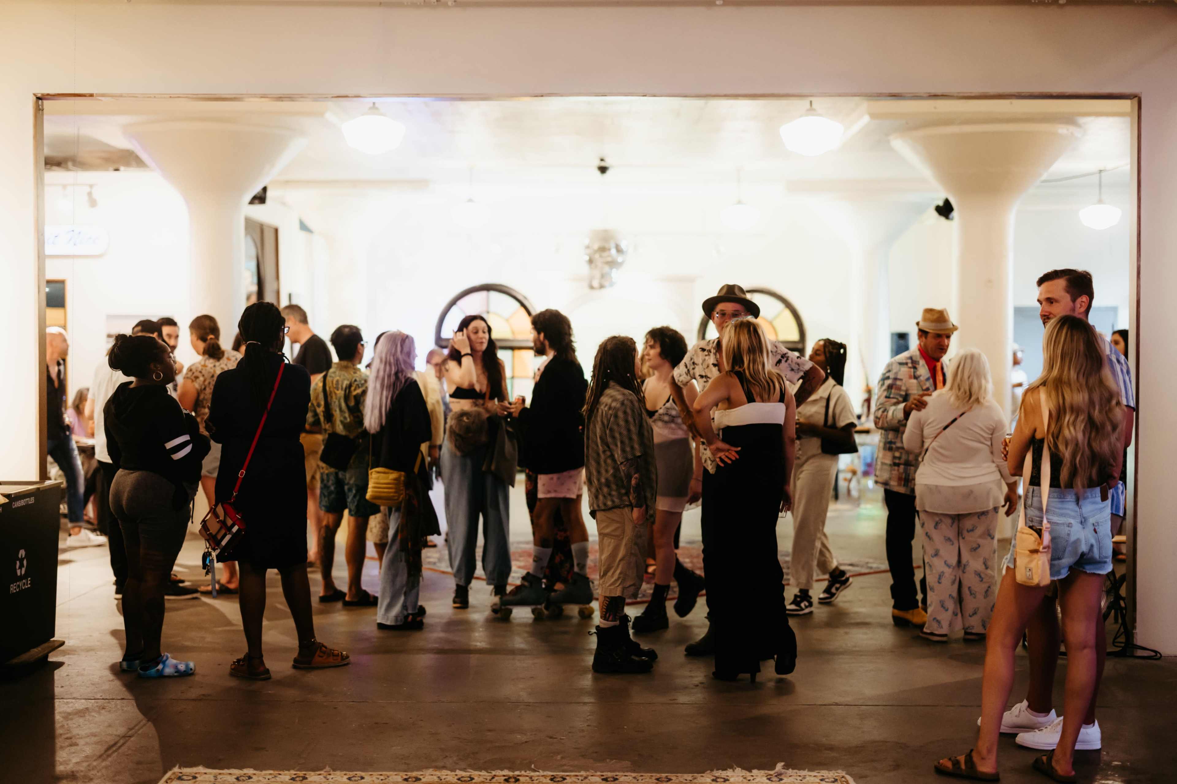 A diverse group of people gathers in a spacious indoor area with white columns and lighting fixtures.