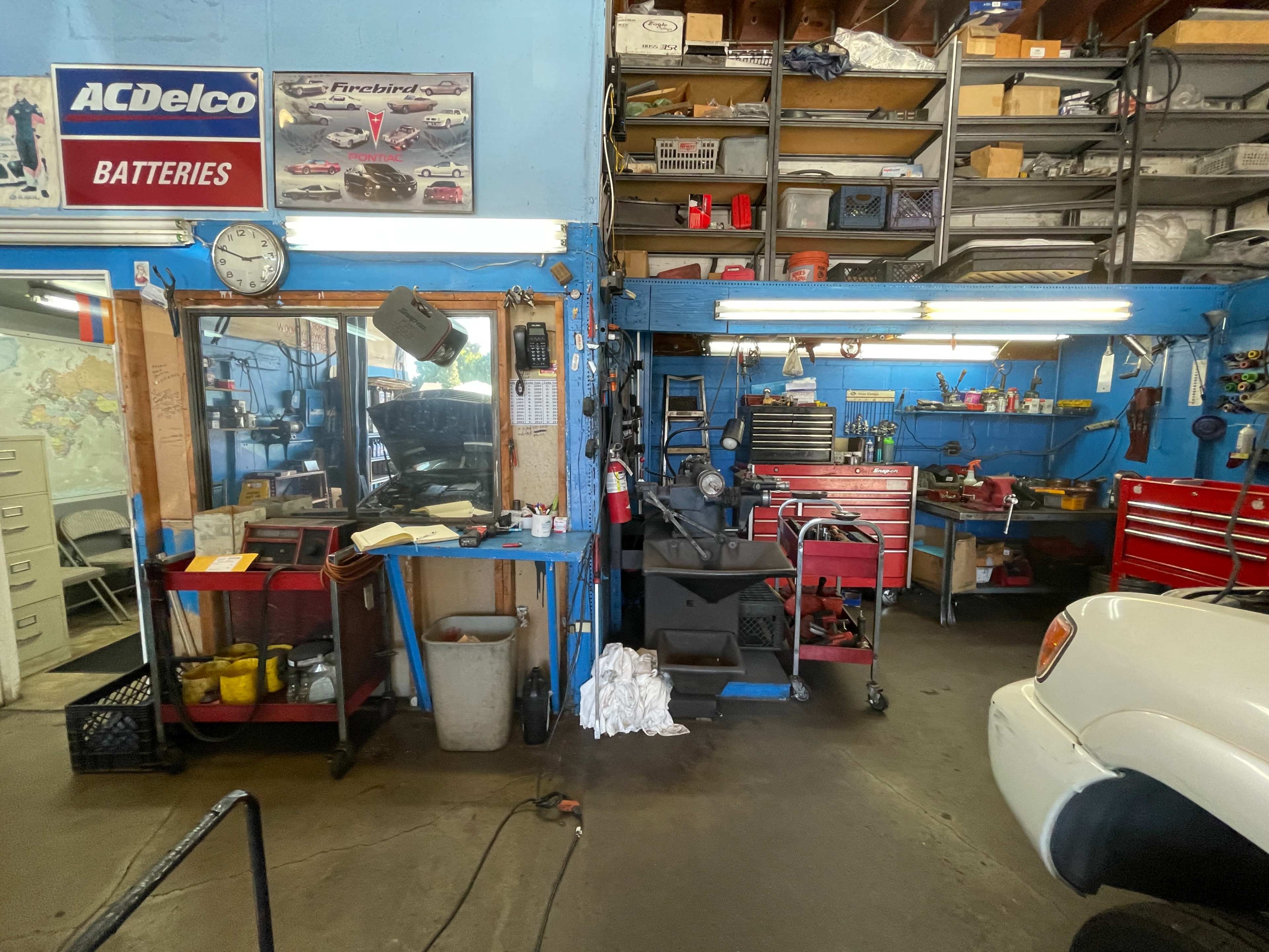 A mechanic's workshop featuring a workbench with tools, cabinets filled with equipment, and a white vehicle parked on a concrete floor.