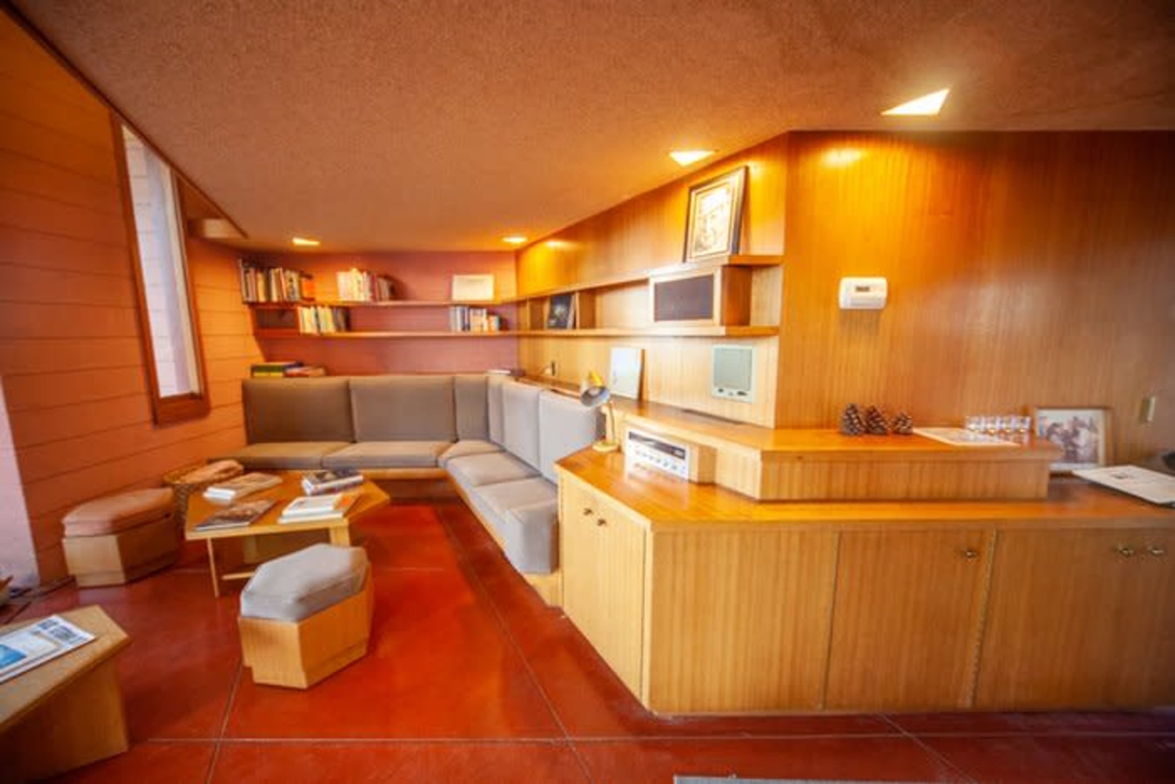 A cozy interior of a mid-century modern room with wooden paneling, a curved sectional sofa, and built-in shelves filled with books.