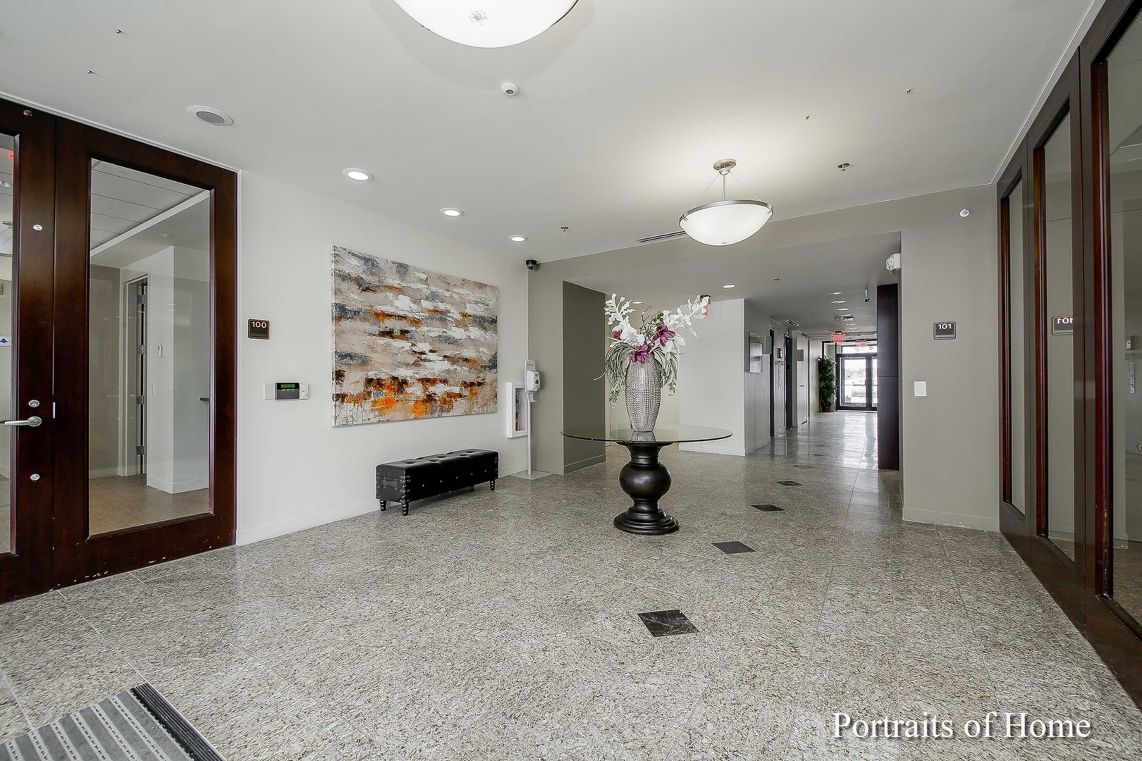 A modern lobby features a decorative wall panel, a large vase of flowers on a pedestal table, and access to various hallways.