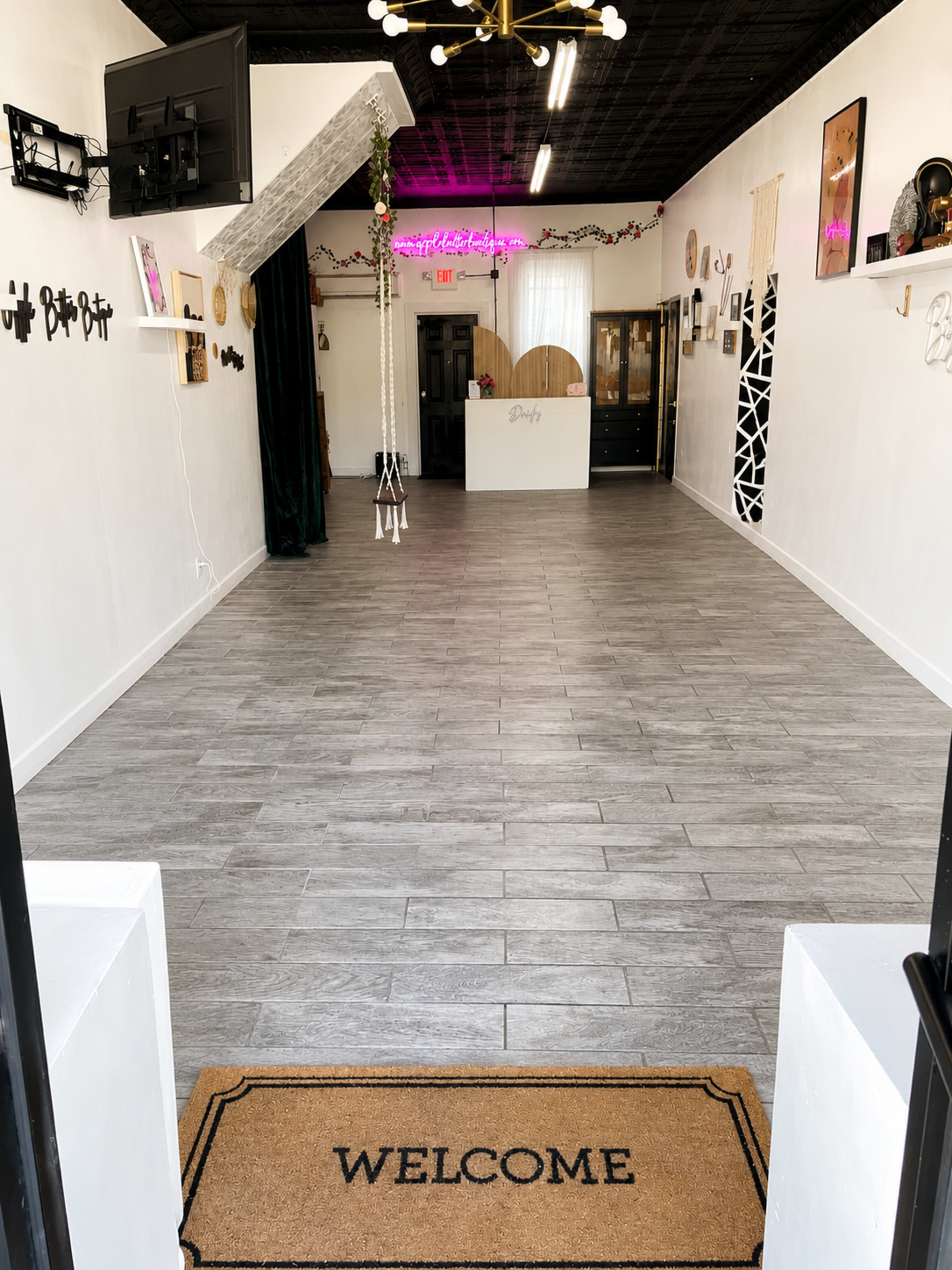 The image shows a spacious, empty interior of a storefront with a welcome mat at the entrance and minimal decorations on the walls.