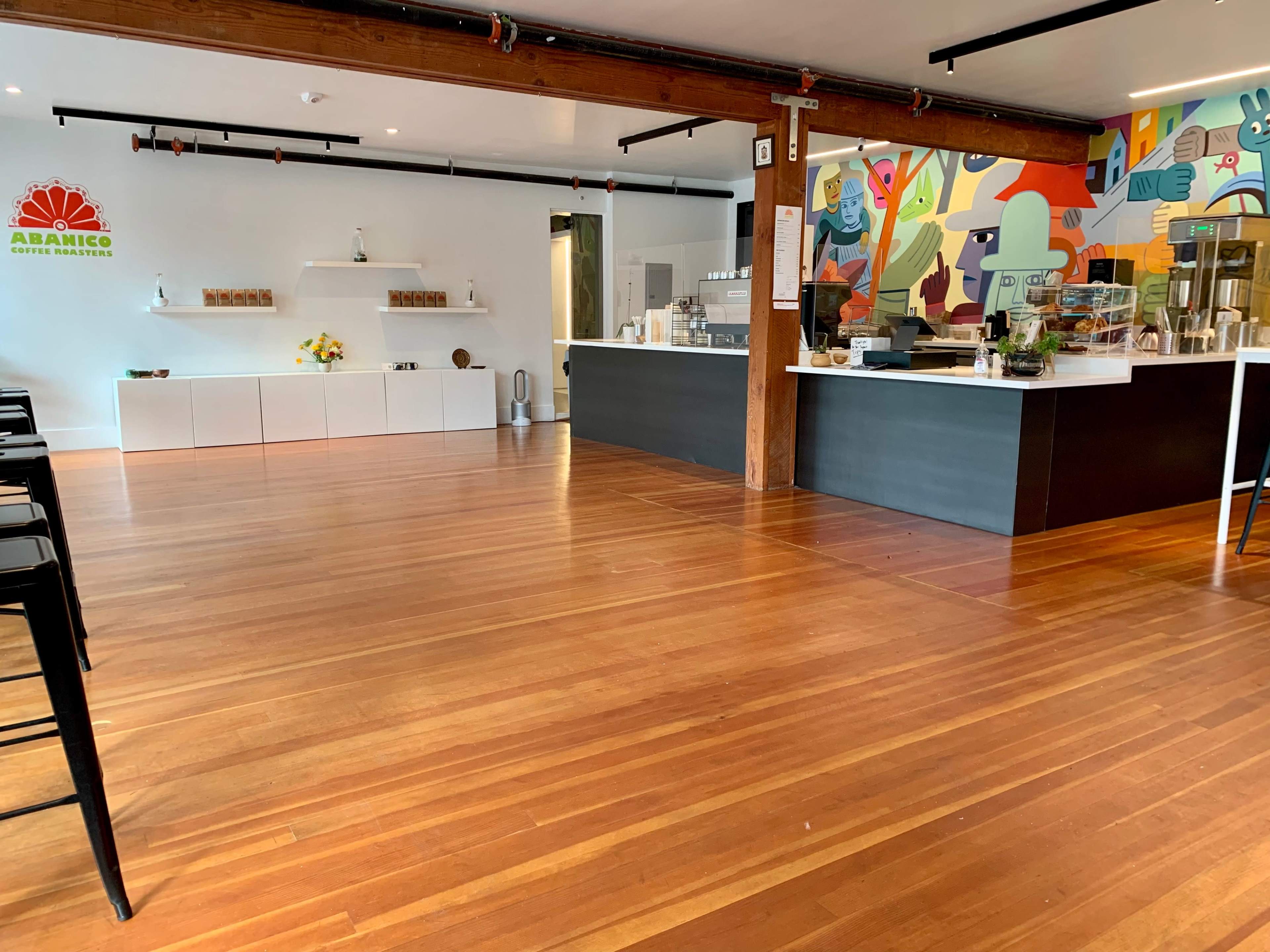The interior of a coffee shop features wooden floors, a bar counter with various coffee preparations, and a colorful mural on the wall.