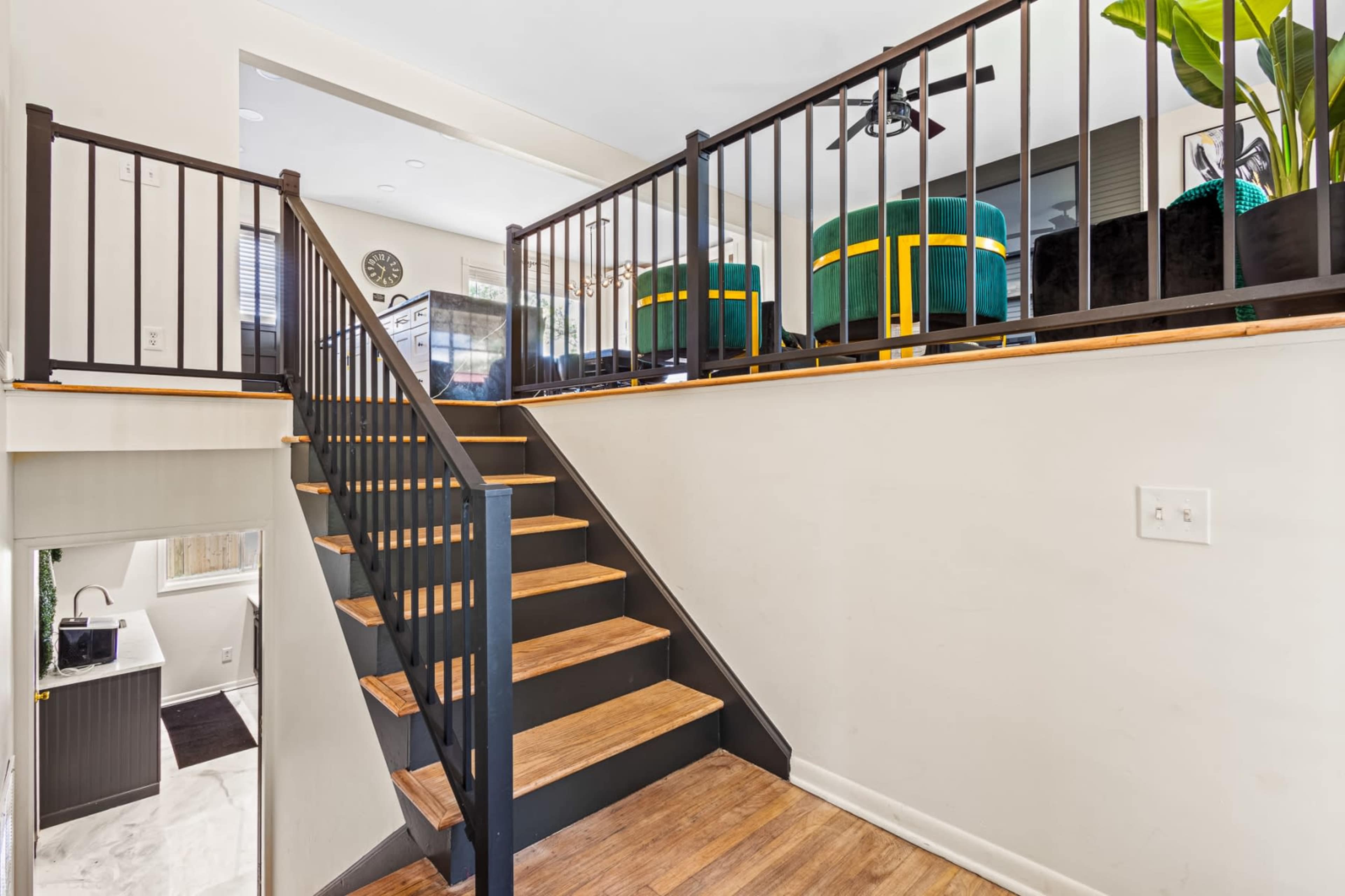 The image shows a staircase leading to an upper level, with a black railing, wooden steps, and a small seating area visible at the top.