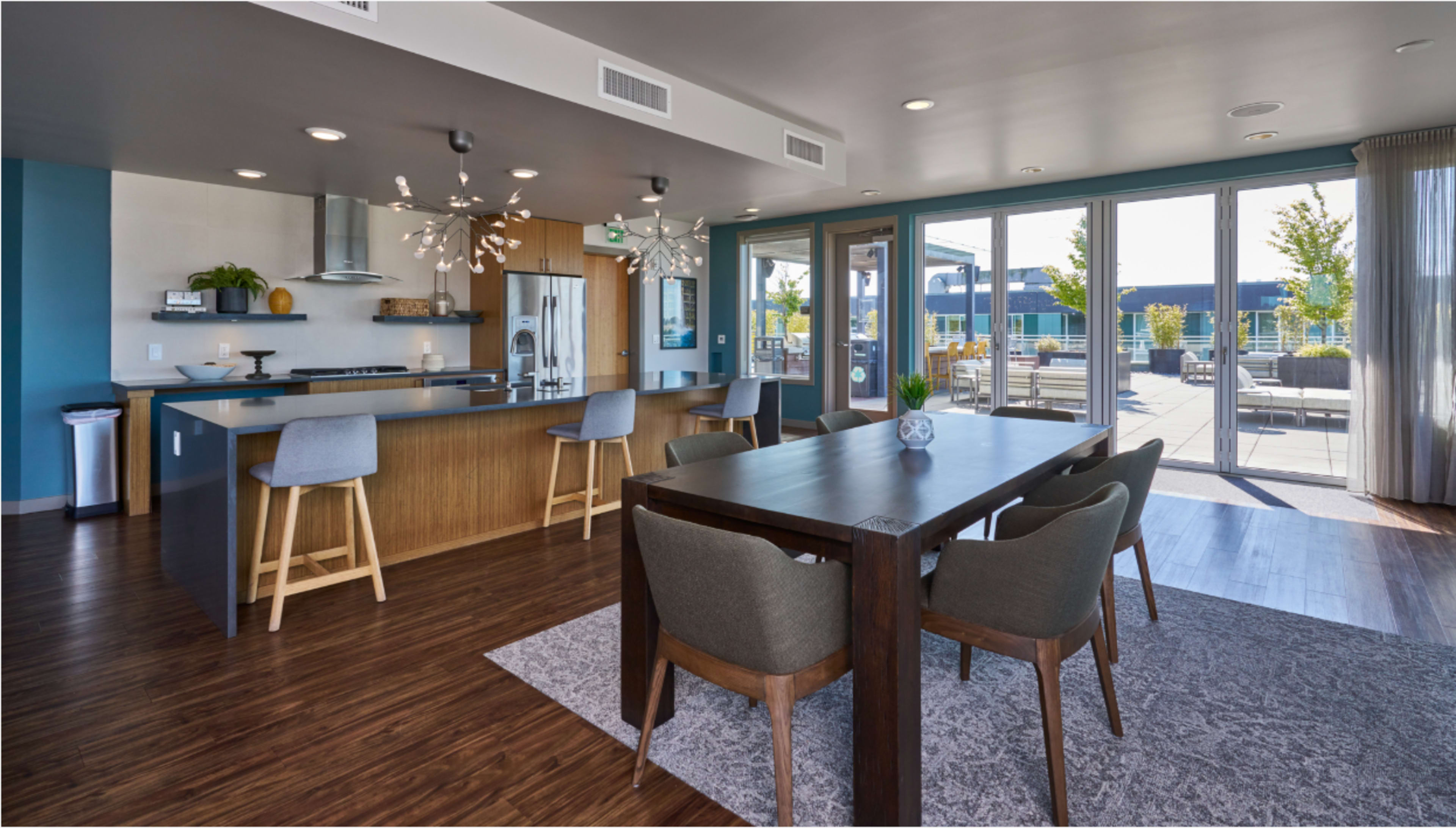 The image shows a modern, open-concept kitchen and dining area with a large table, chairs, and sliding glass doors that open to an outdoor patio.