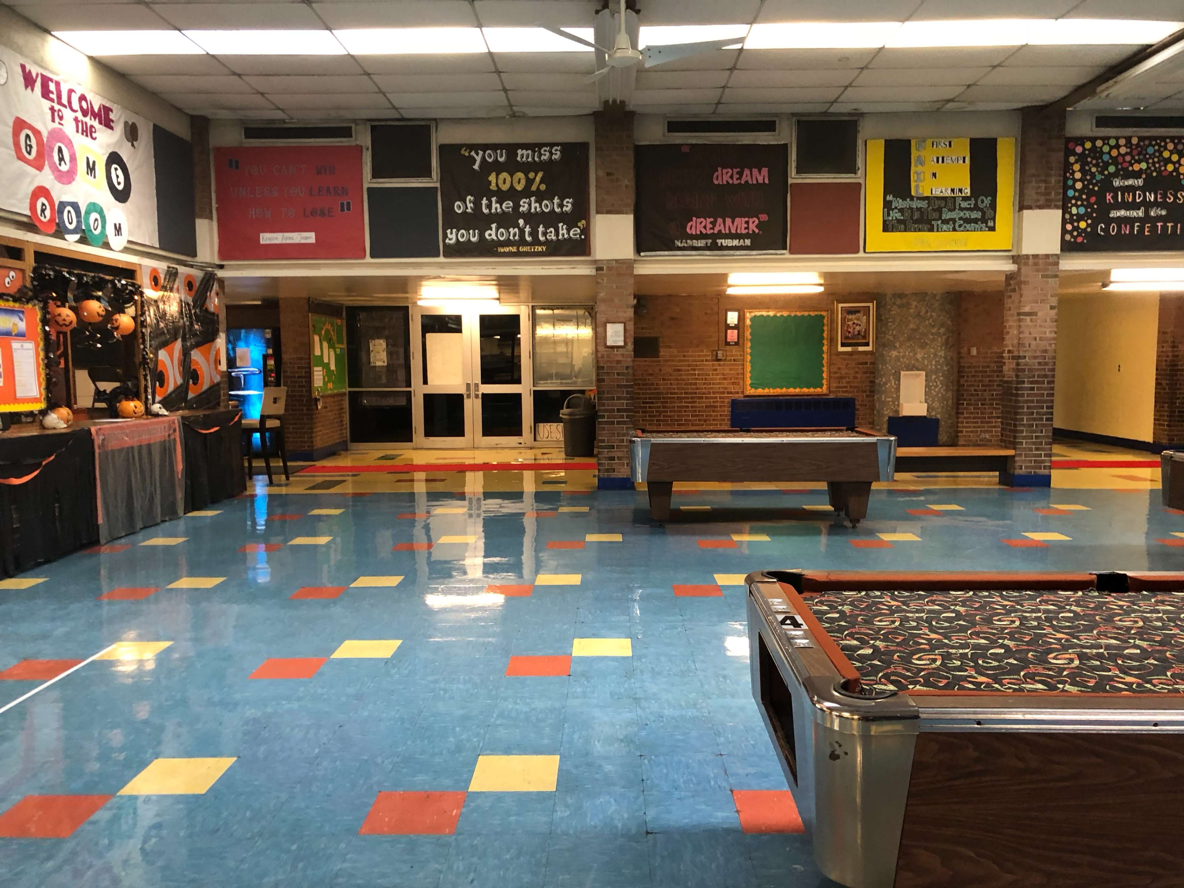 A brightly colored school hallway with game tables and posters on the walls promoting motivational messages and school spirit.