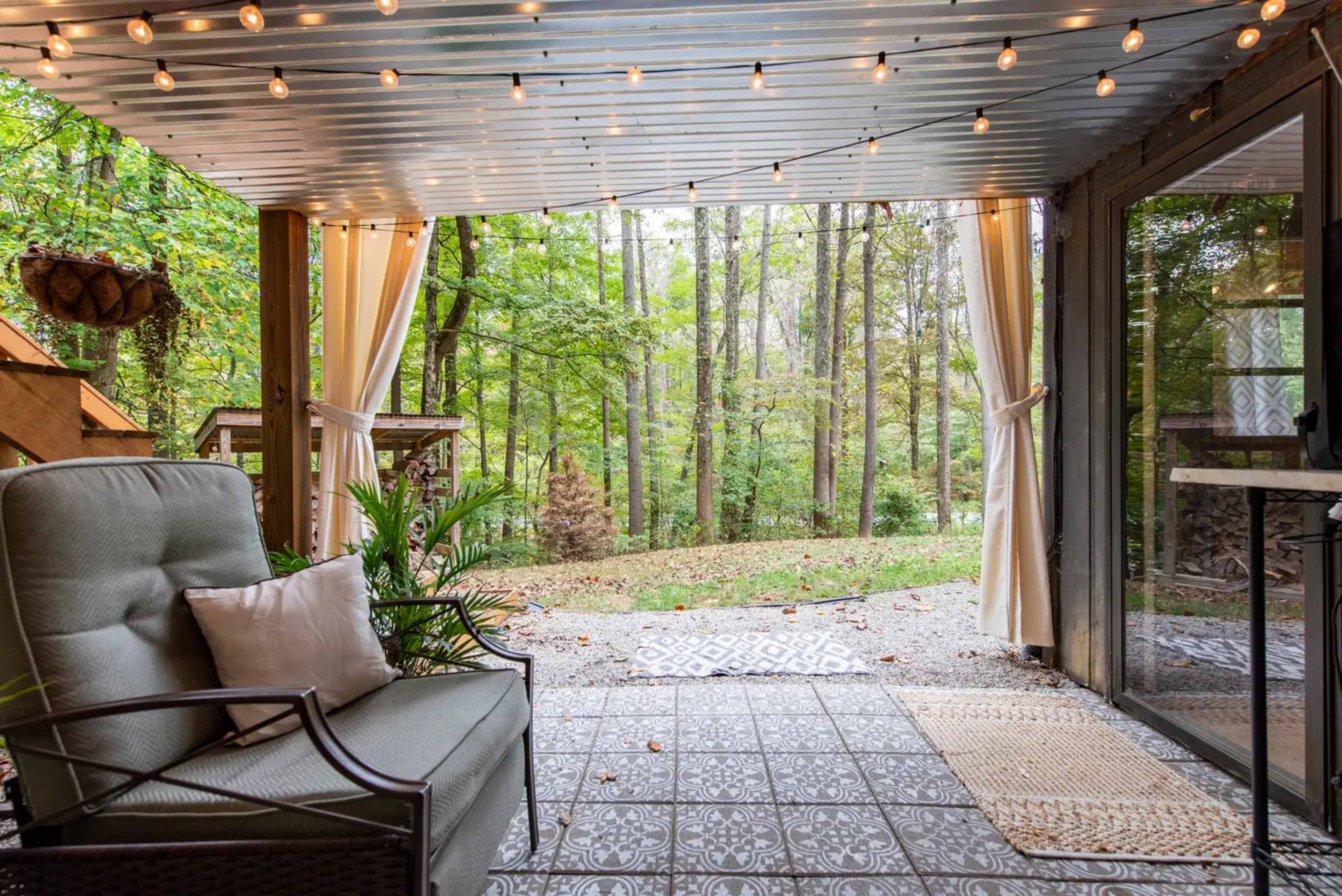 A cozy outdoor seating area with string lights and a view of a wooded landscape.