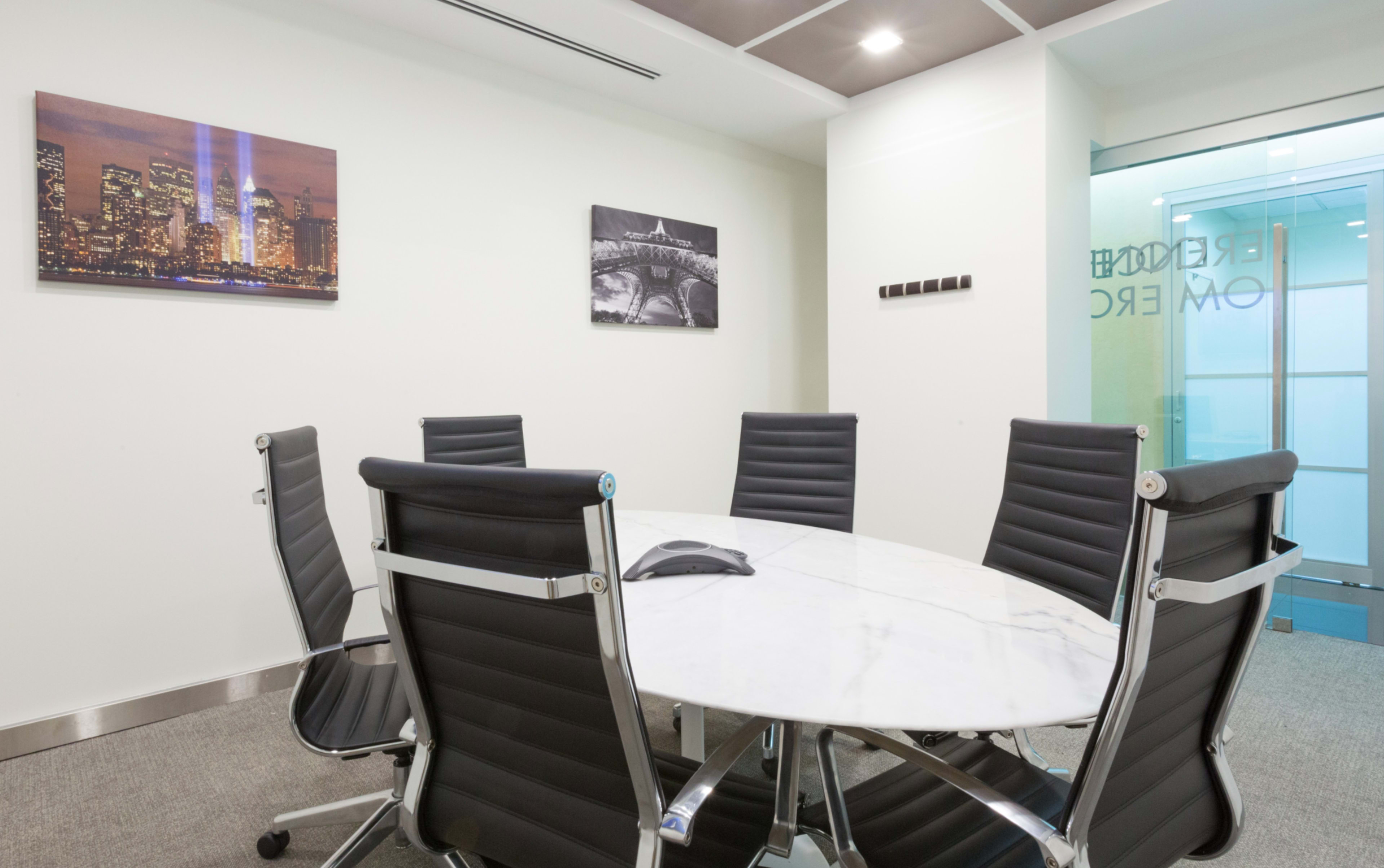 A modern conference room features a round marble table surrounded by black leather chairs and glass walls.