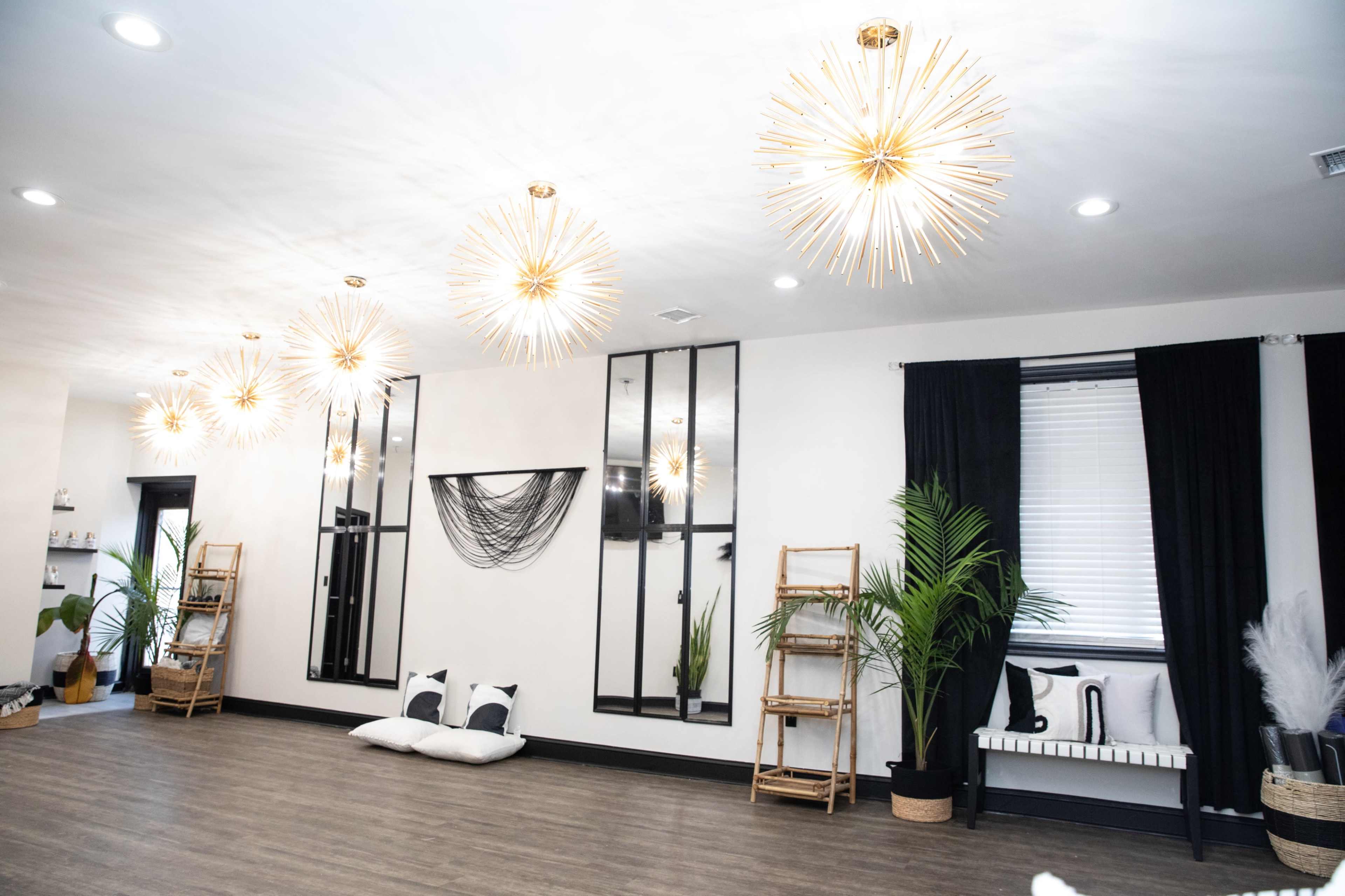 The room features modern lighting fixtures, mirrors, and bamboo shelves, arranged around a minimalist decor with plants and seating areas.
