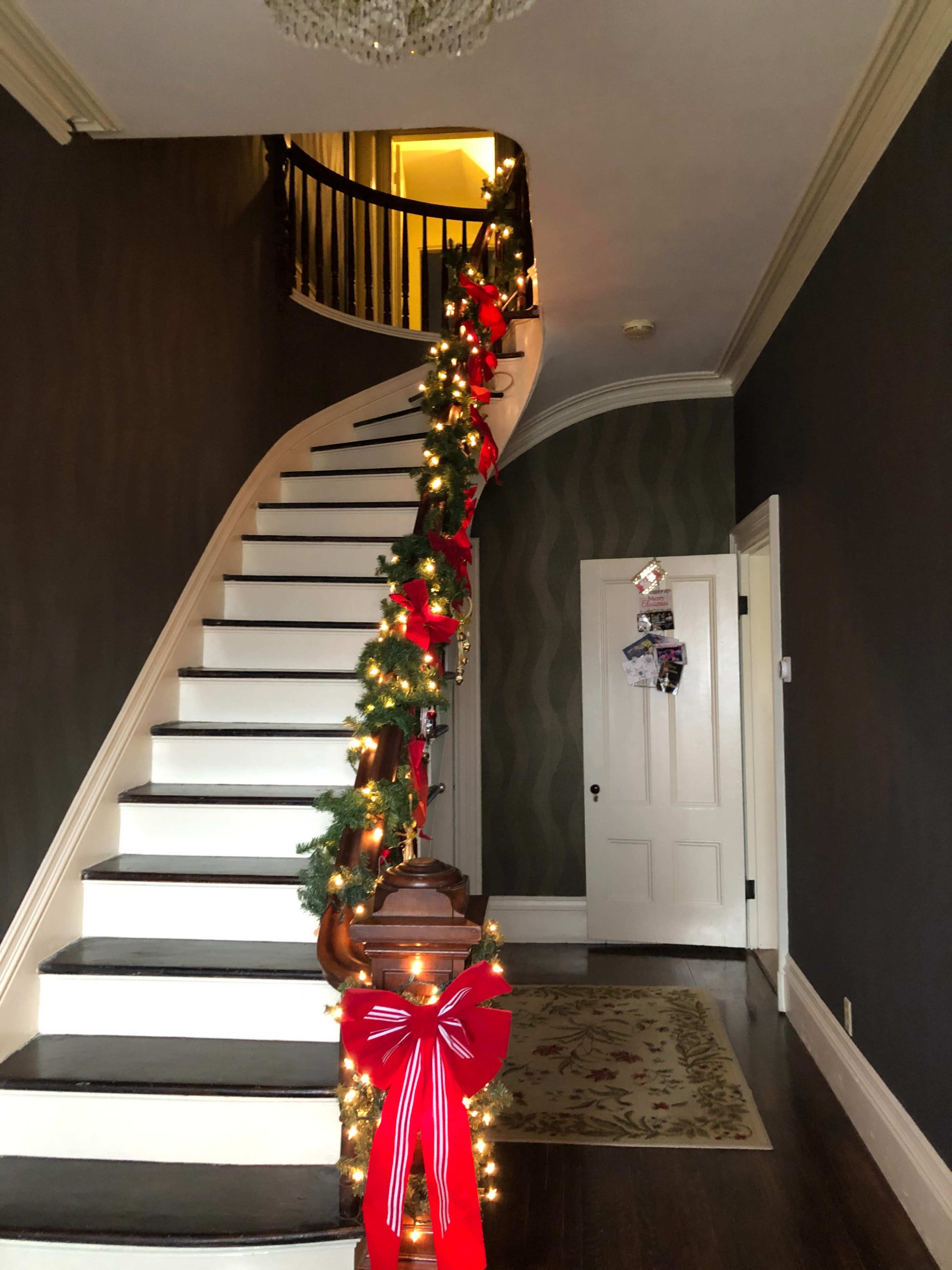 A spiral staircase is decorated with garlands and red bows, leading to a doorway at the top.