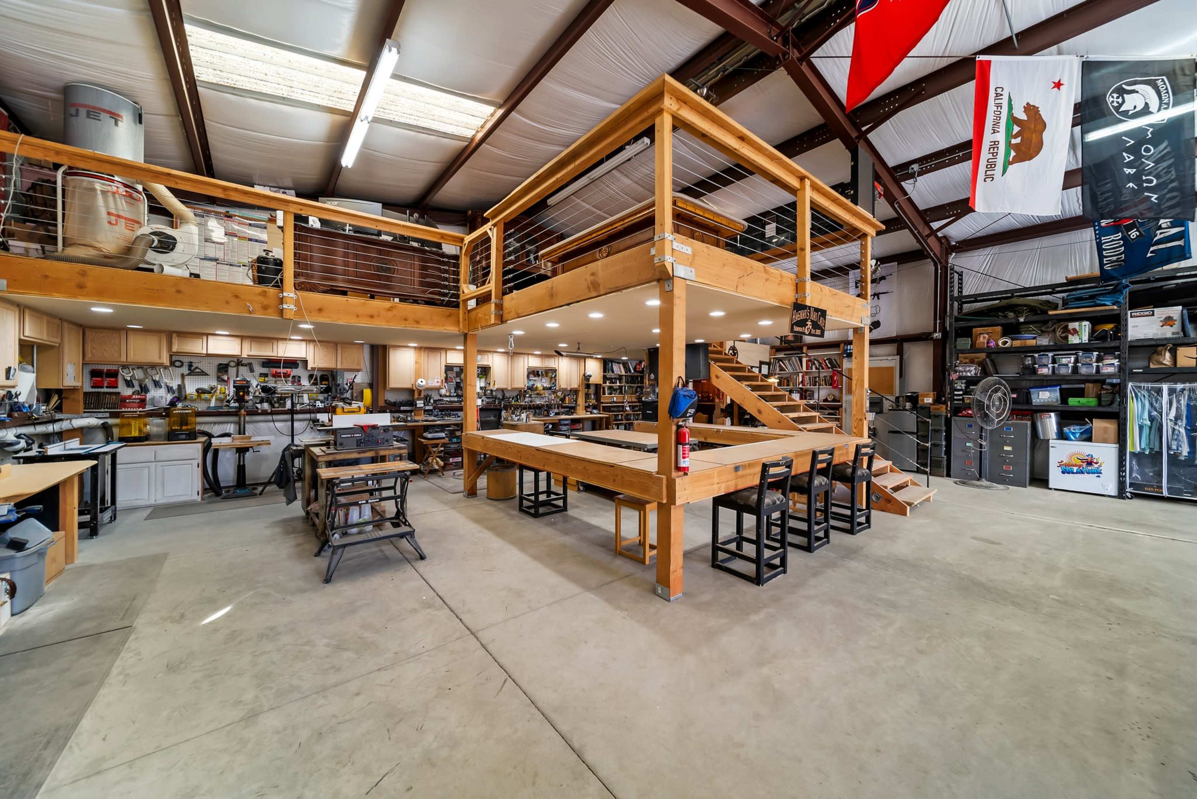 The image shows an industrial workshop with two levels, featuring workbenches, tools, and various organized equipment.