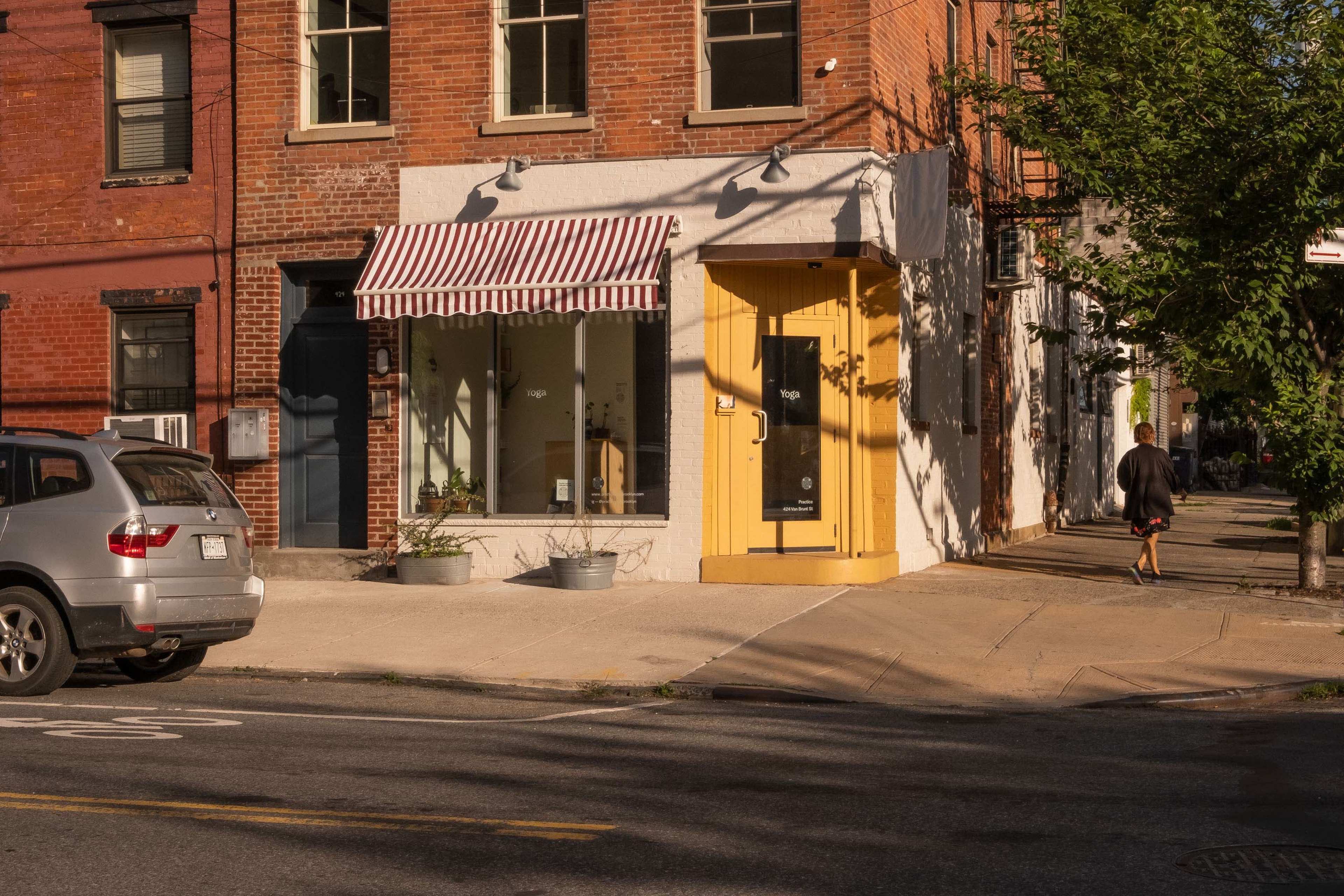 A gray SUV is parked on the street in front of a brick building with a yellow door and a shop window featuring an awning.