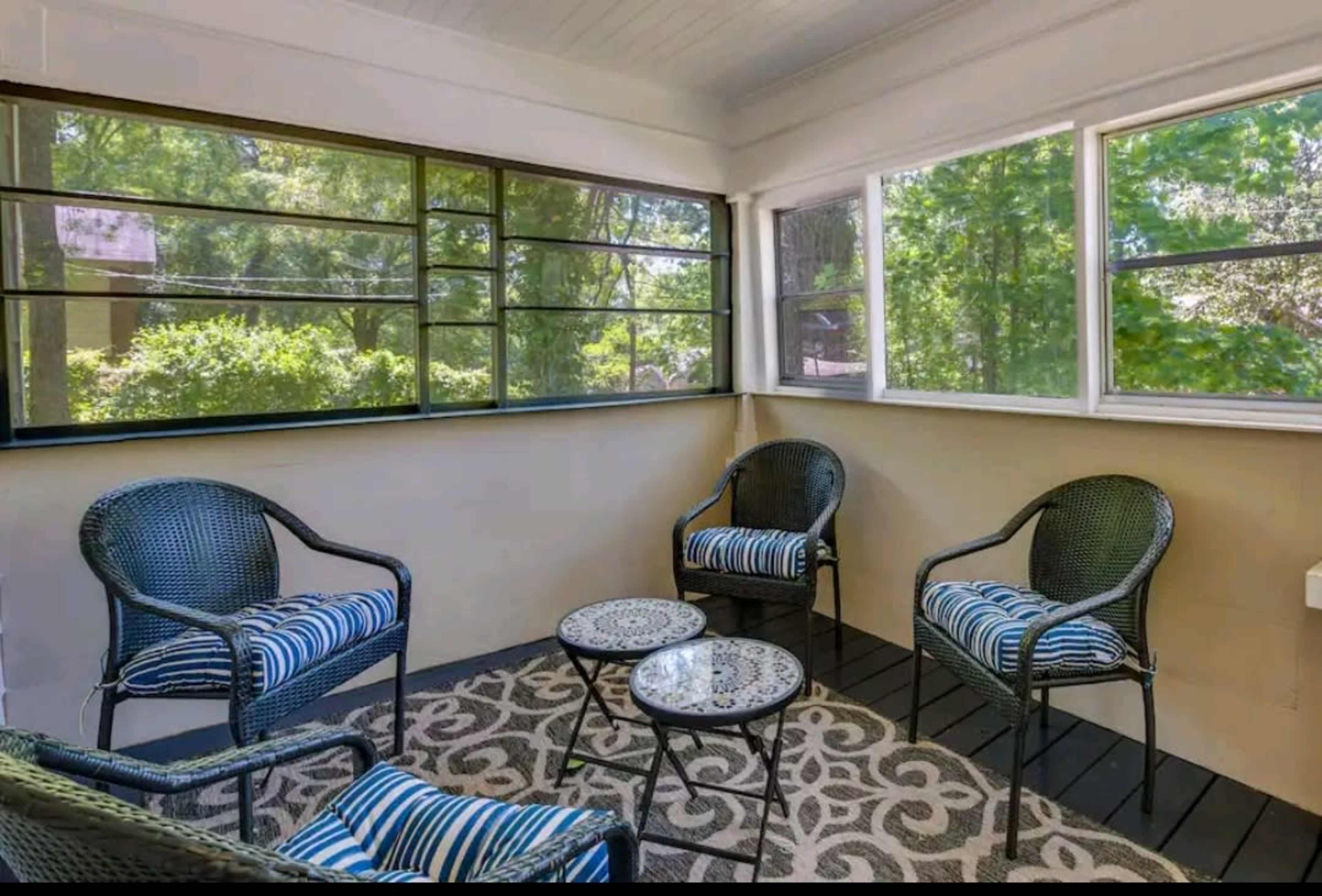 A screened porch features four wicker chairs with blue and white striped cushions surrounding a round table on a patterned rug.