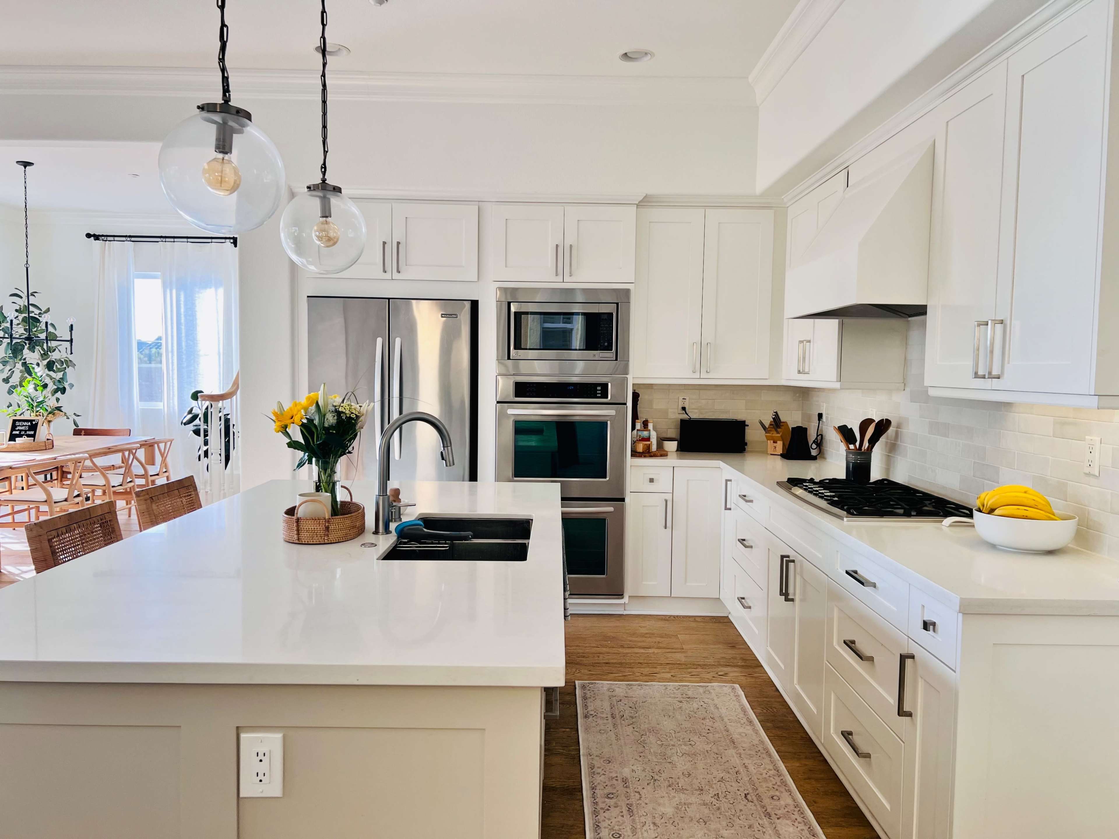 A modern kitchen featuring white cabinetry, stainless steel appliances, and a central island with a sink and elegant lighting fixtures.