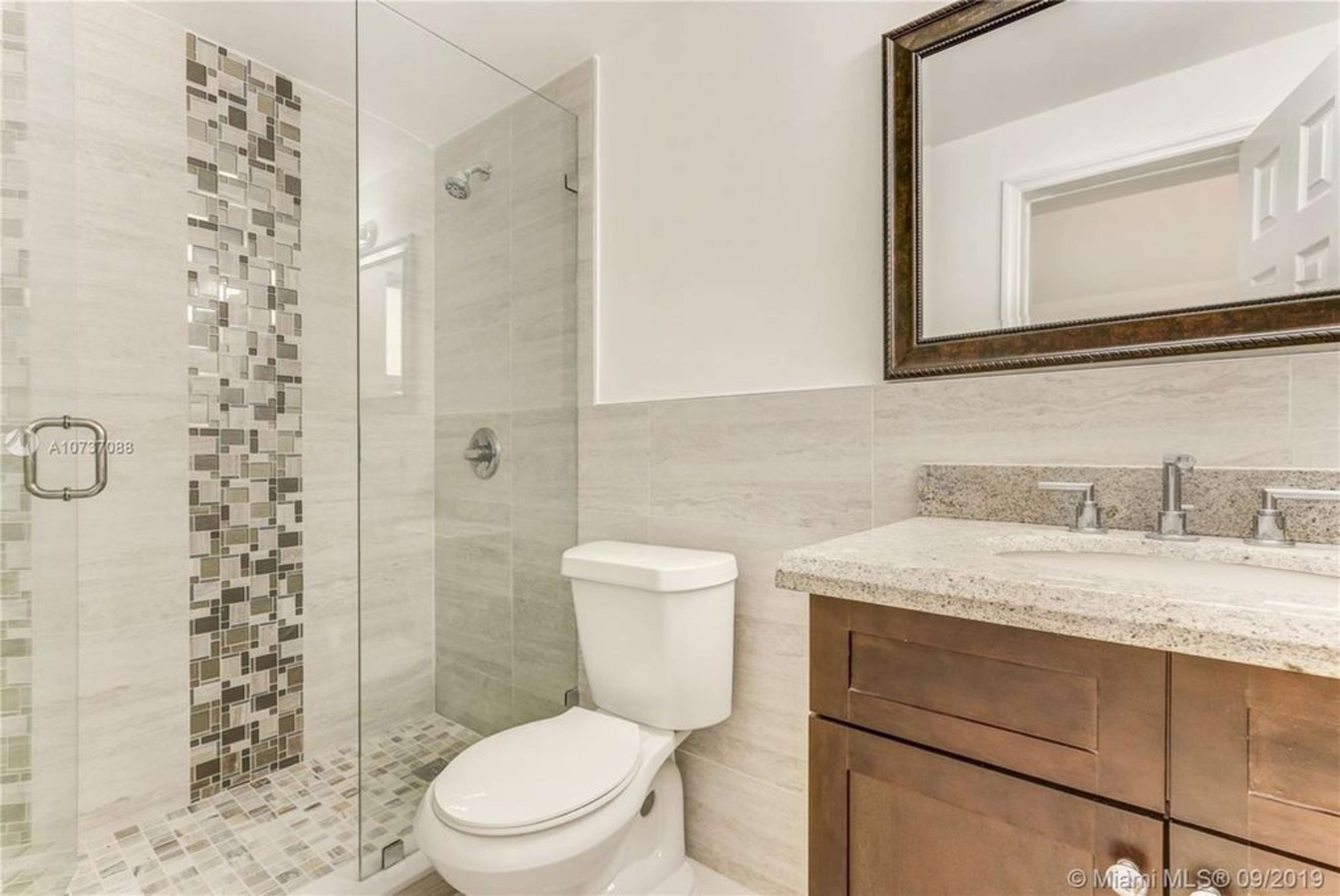 A modern bathroom featuring a glass shower, a toilet, and a vanity with a countertop and sink.