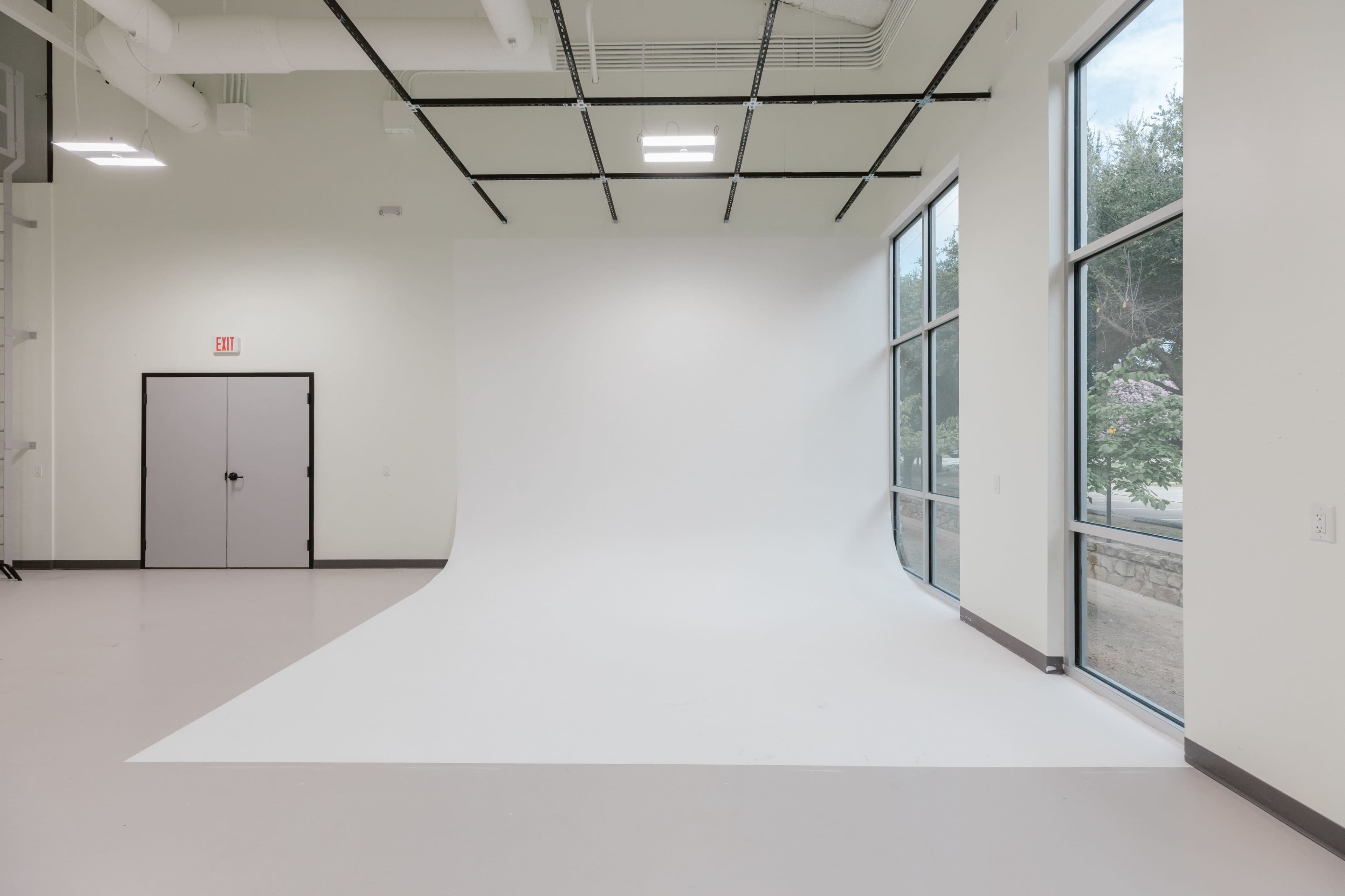 The image features a spacious room with a seamless white backdrop, large windows, and a gray door on one wall.
