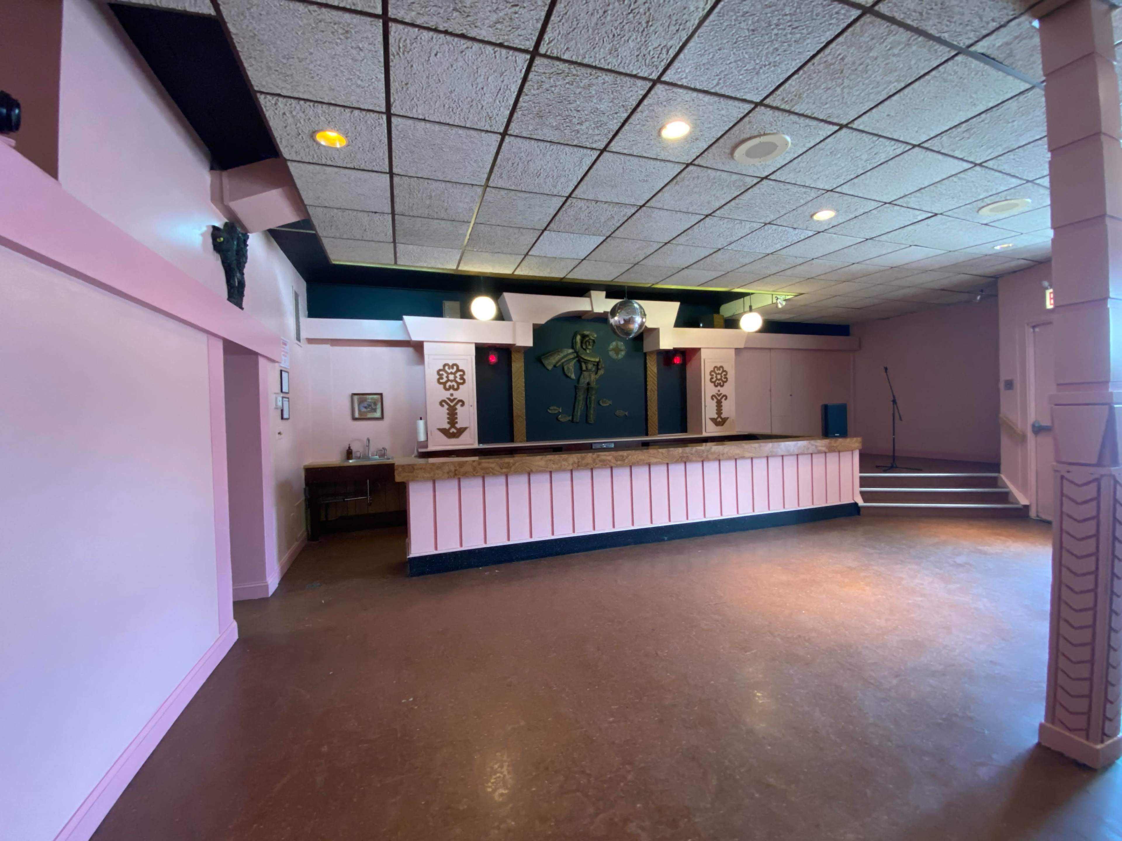 A vacant reception area with a pink-painted wall, a counter, and a small stage in the background.