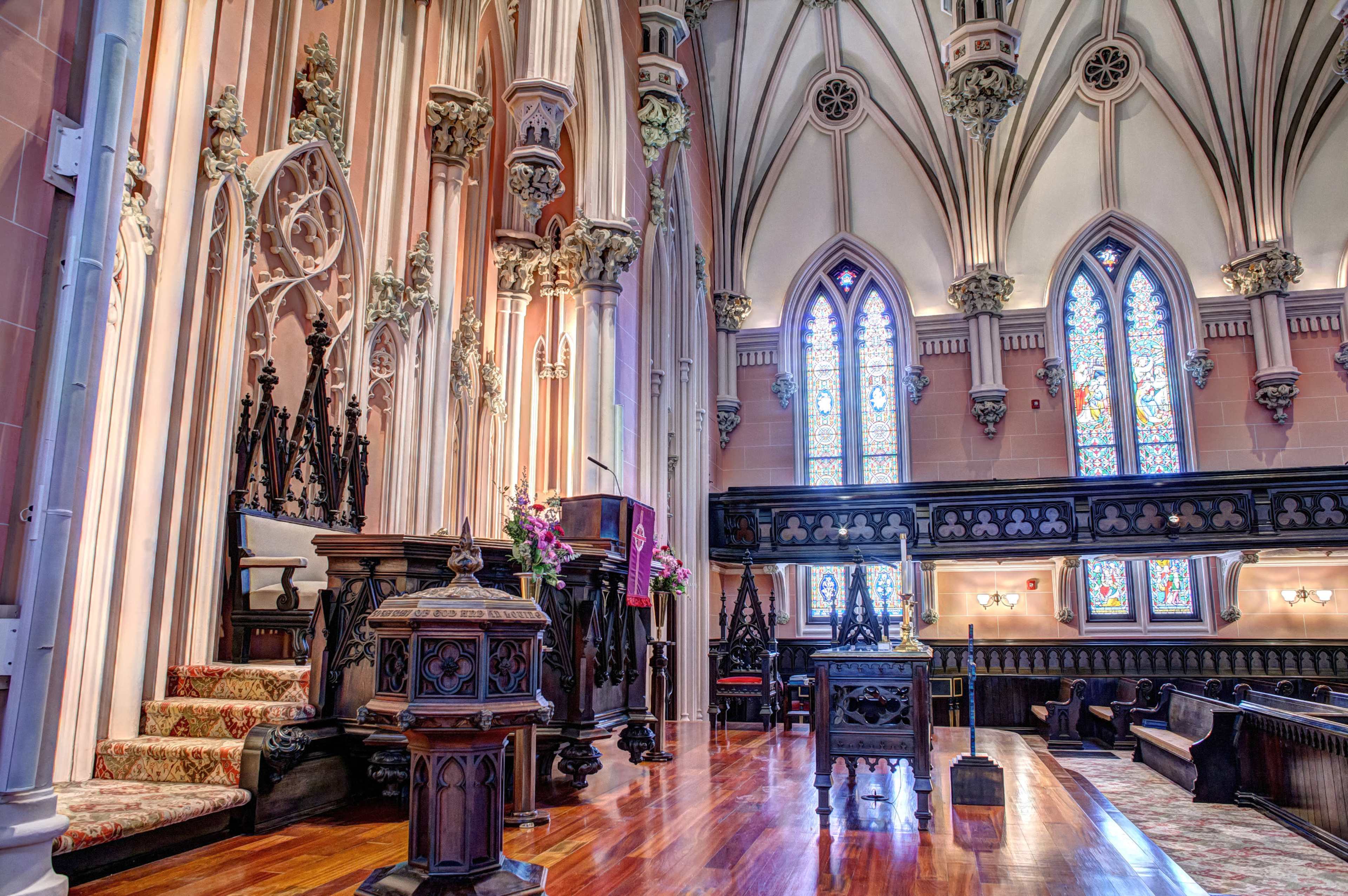 The interior of a church features ornate woodwork, stained glass windows, and a raised altar area with seating.