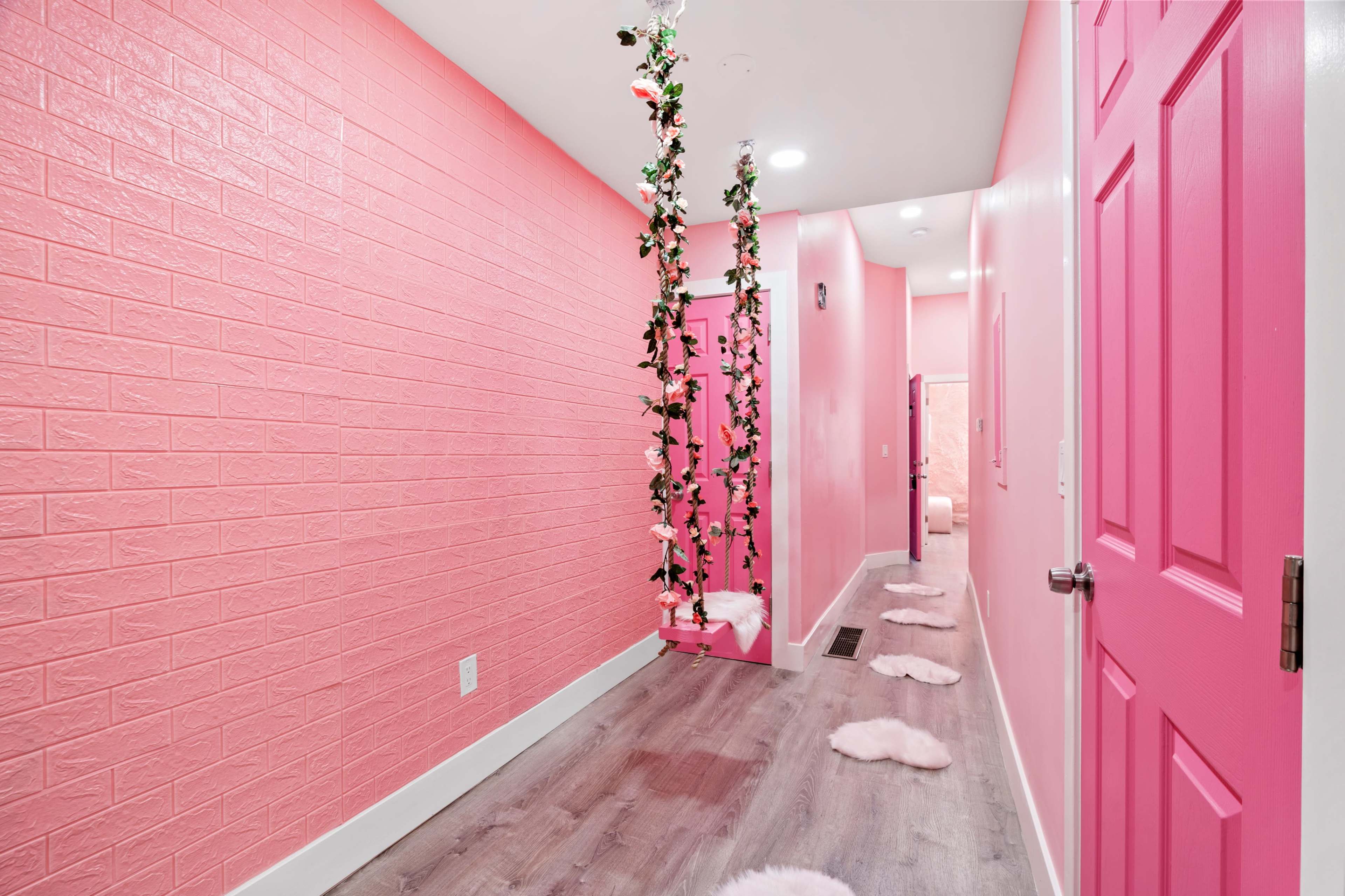 A pink hallway features a hanging swing adorned with greenery and fluffy rugs along the floor.