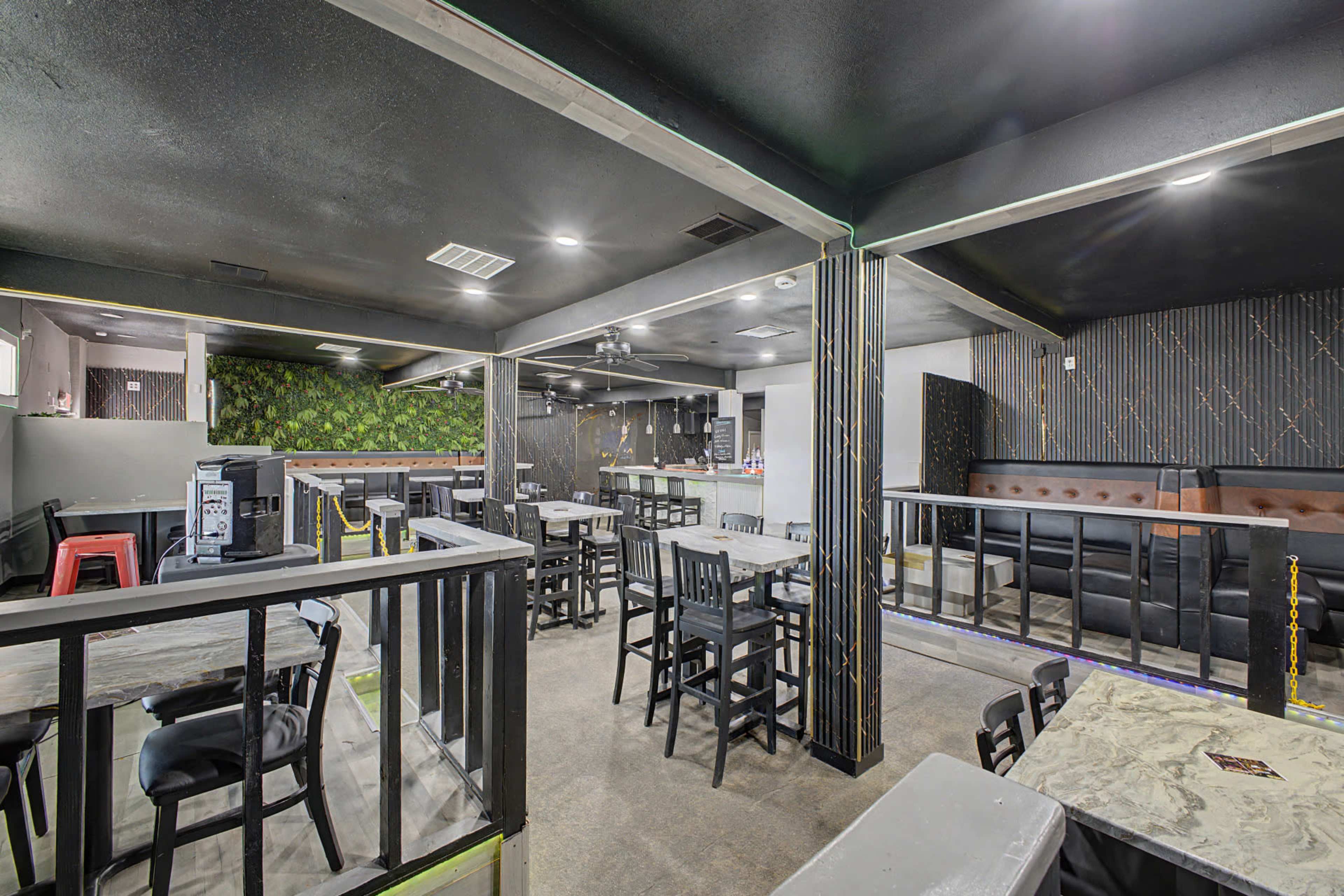 The image shows a modern restaurant or lounge interior with black and gray decor, seating arrangements, and a bar area in the background.