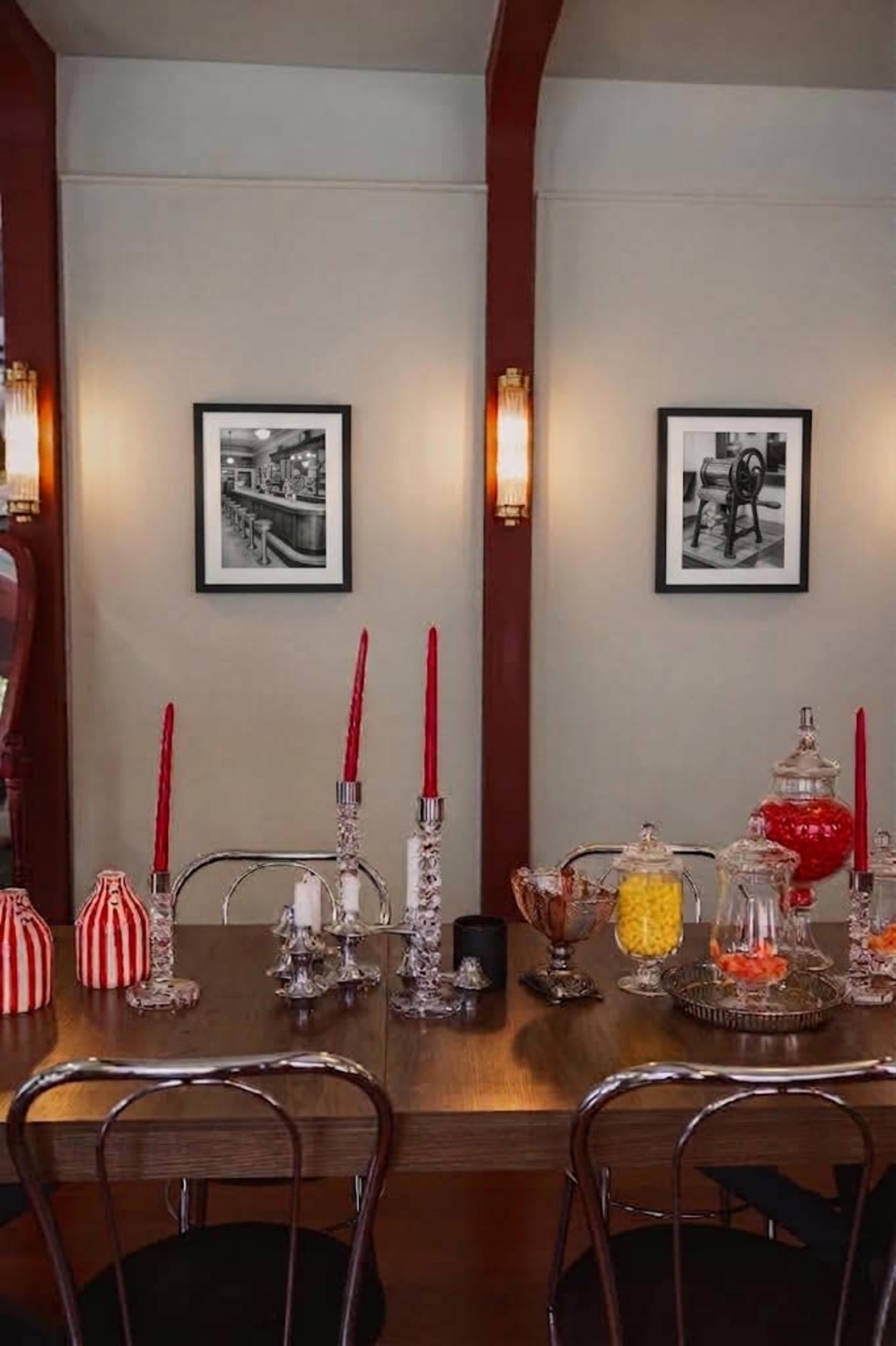 A dining table is set with red candles and decorative jars, flanked by black and white photographs on the walls.