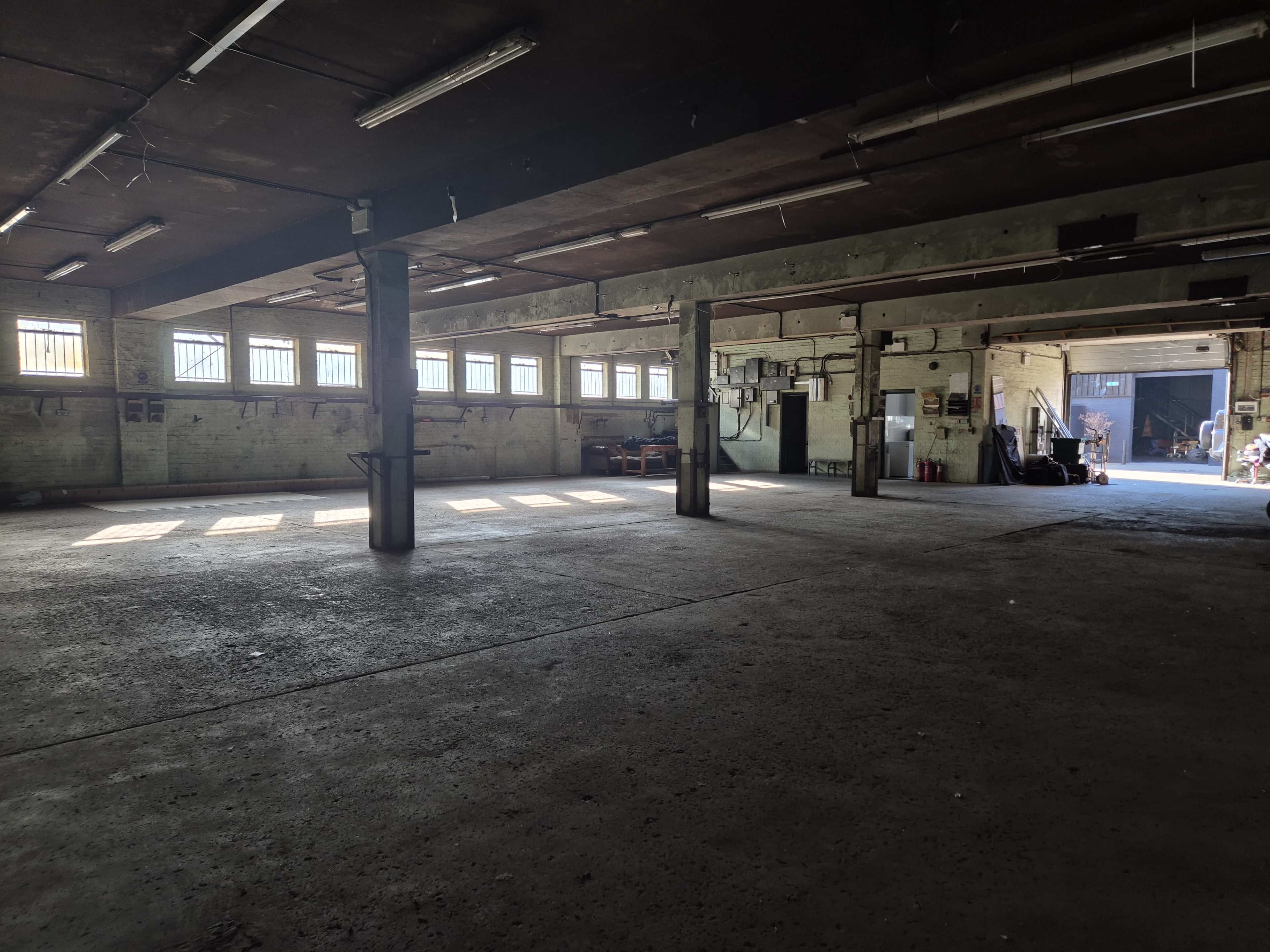 The image shows an empty industrial space with concrete flooring and large windows along the walls.
