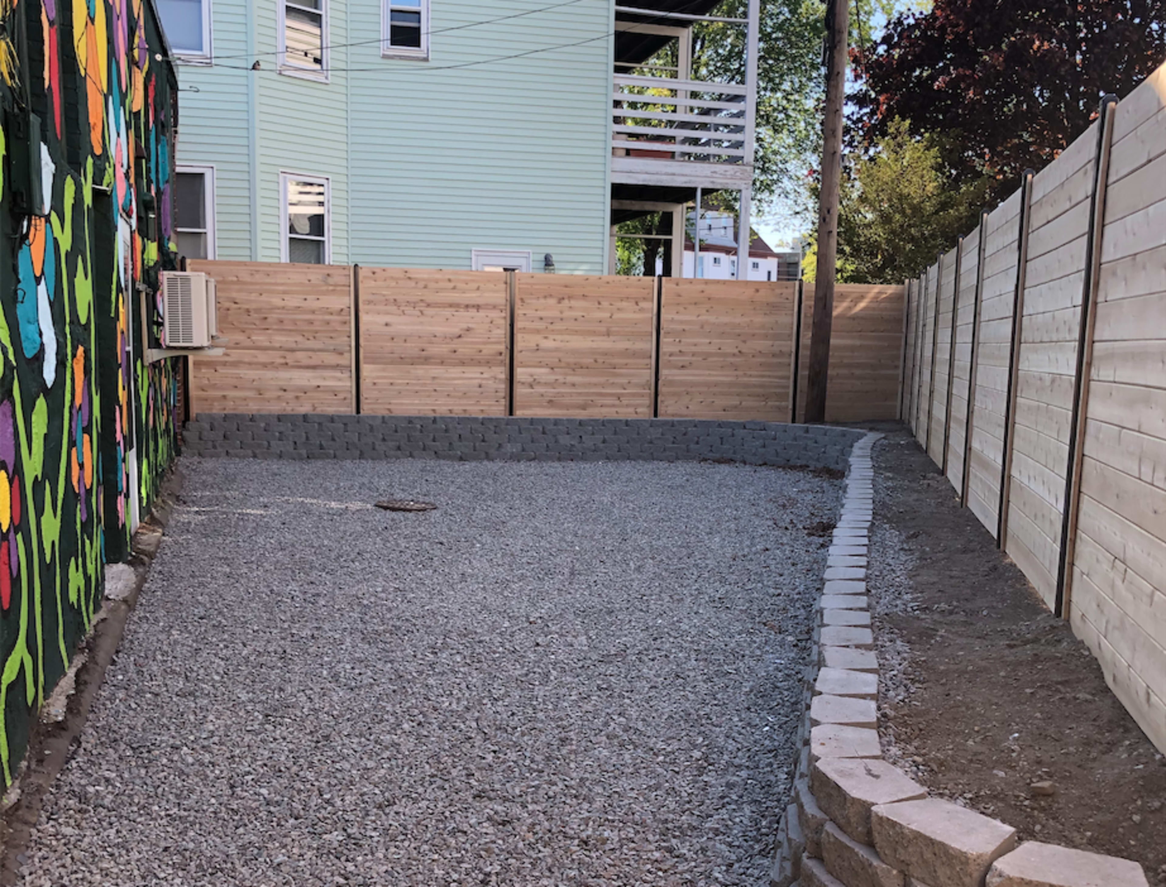 A gravel area enclosed by wooden fencing, with a colorful mural visible on one side.