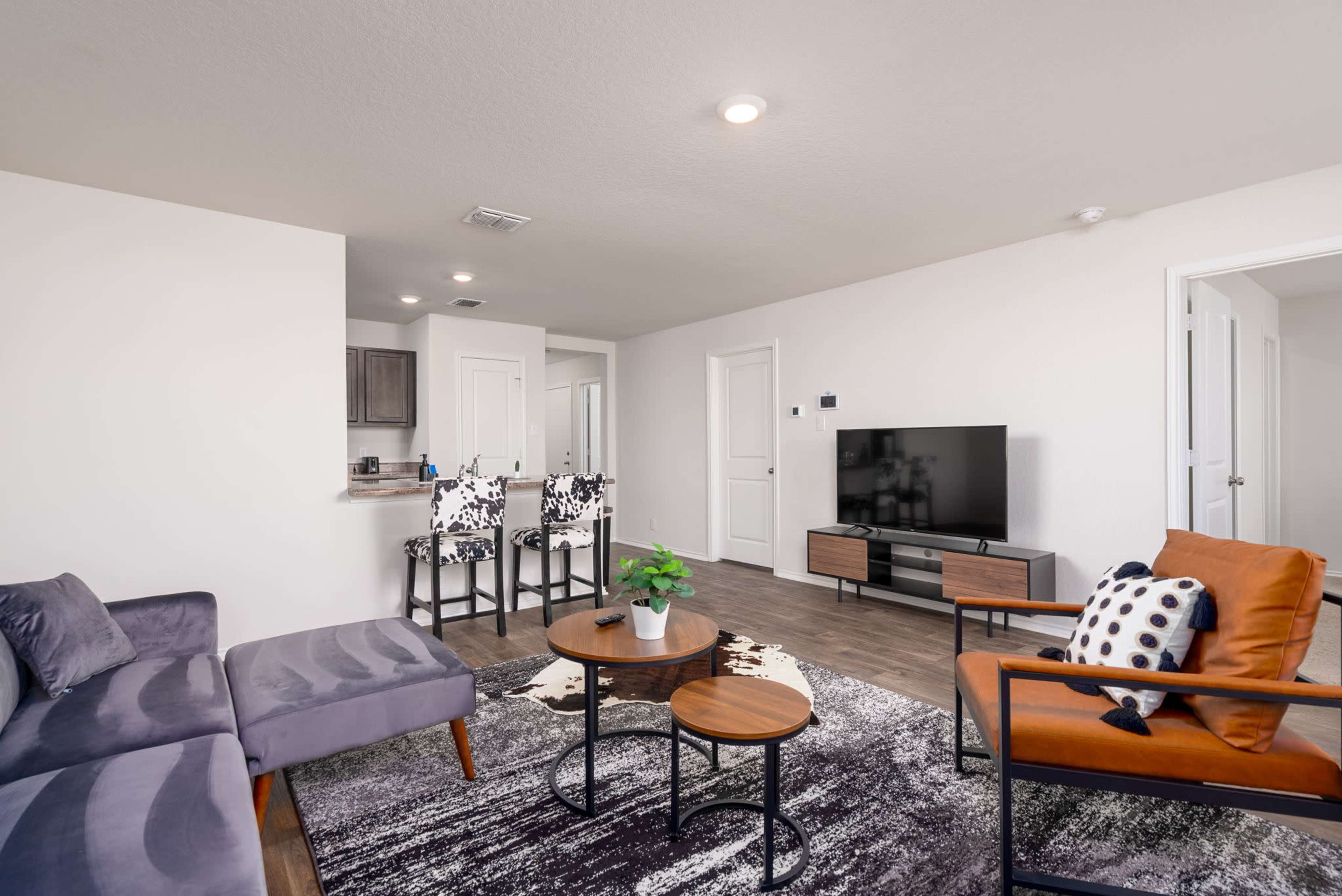A modern living room with a gray sofa, two round coffee tables, an orange chair, and a television on a stand, all set against a light-colored wall.