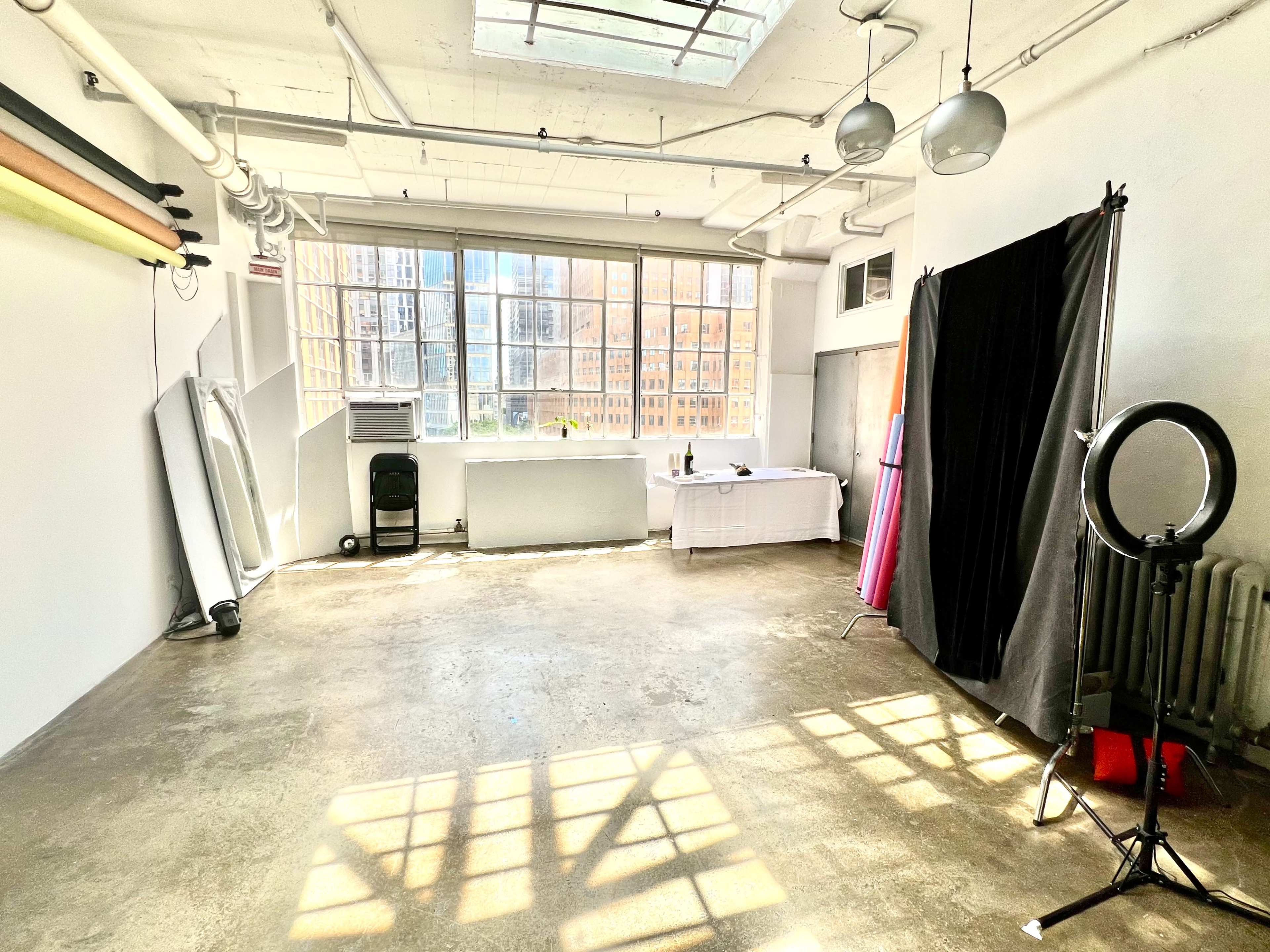 A spacious studio with large windows, a white table, and various lighting equipment set up for a photoshoot.