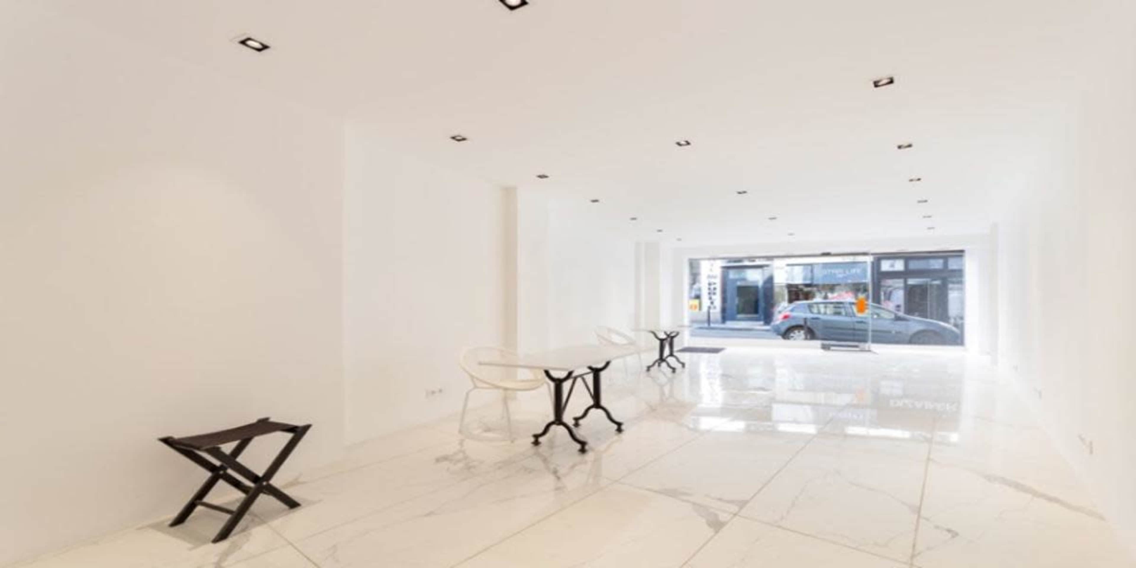 The image shows a minimalist interior space with white walls and a shiny marble floor, featuring a table and chairs, and a large window displaying an outside street view.