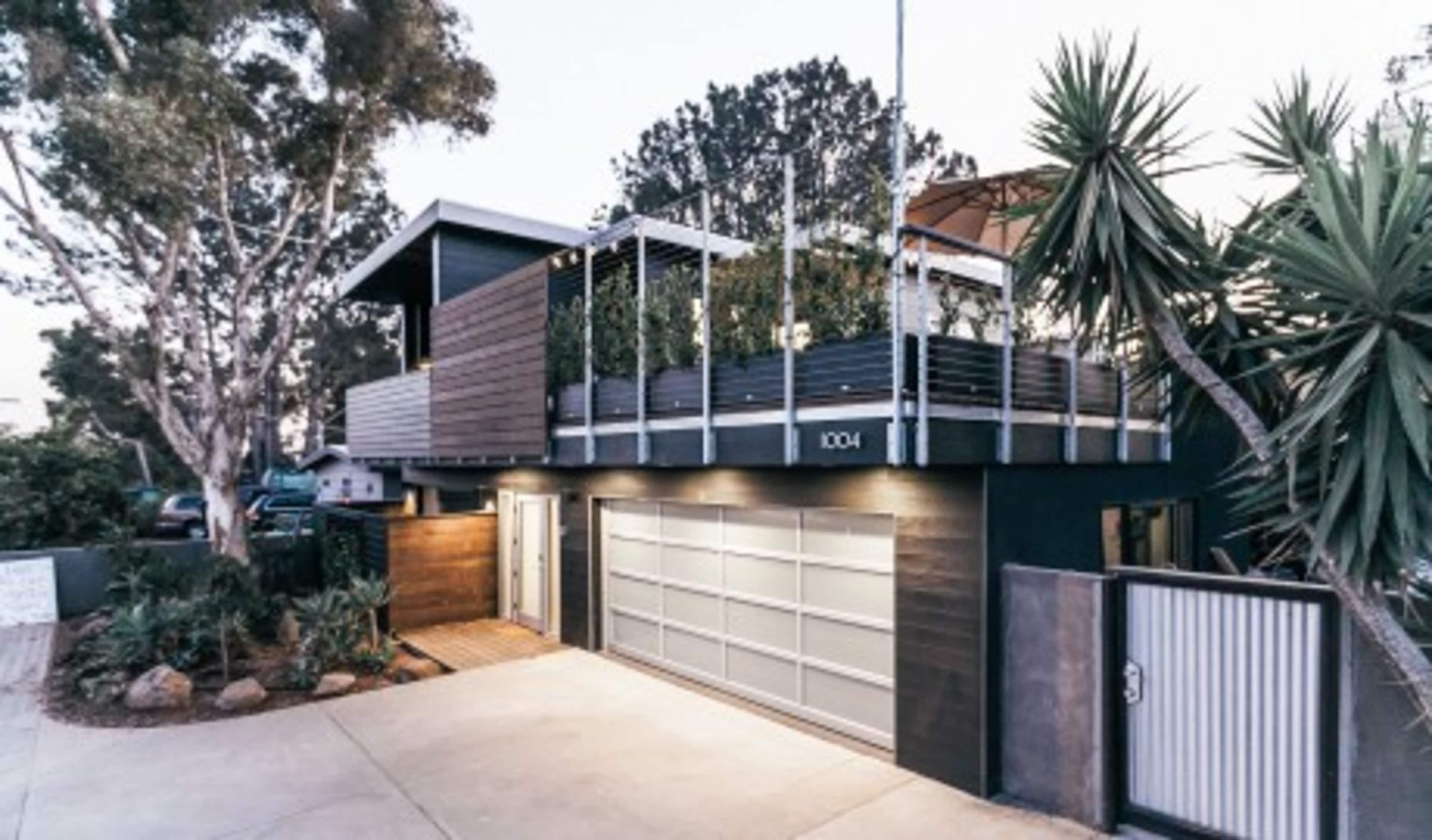 The image shows a contemporary two-story house with a landscaped rooftop garden and a garage door in the front.