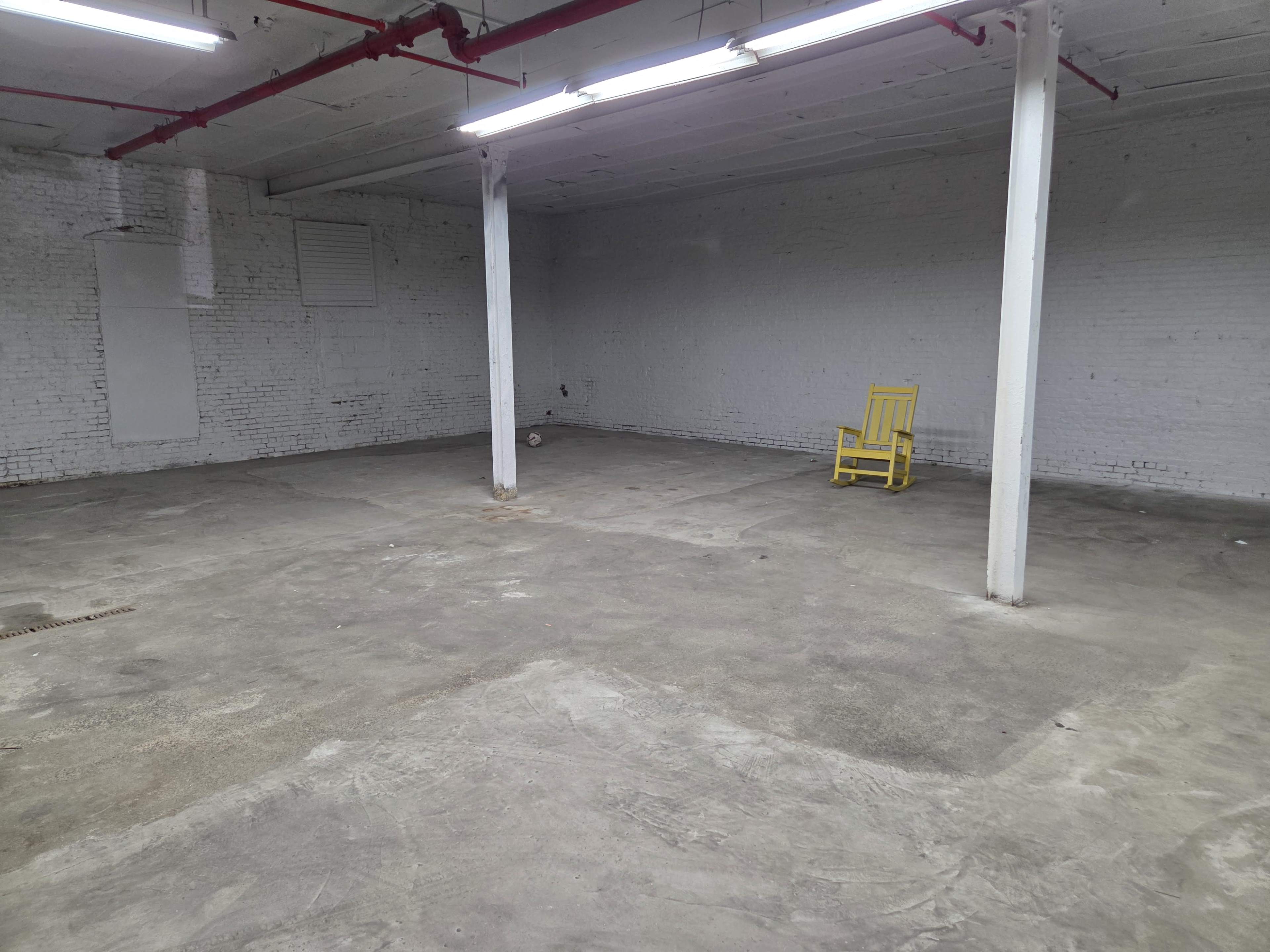 An empty room with a concrete floor, white brick walls, and a single yellow chair in the corner.
