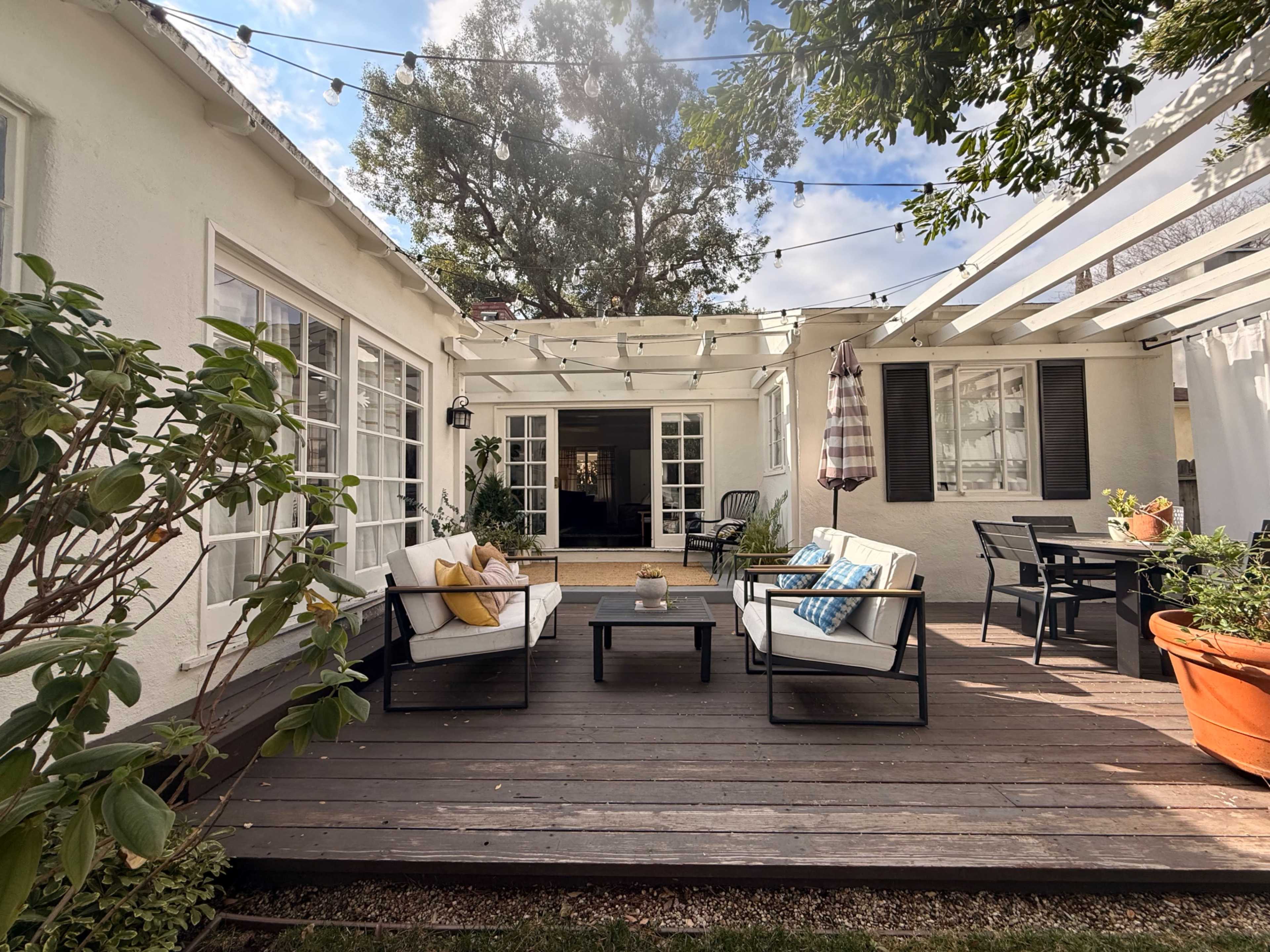 The image shows a backyard patio area with outdoor seating, a table, and string lights overhead.