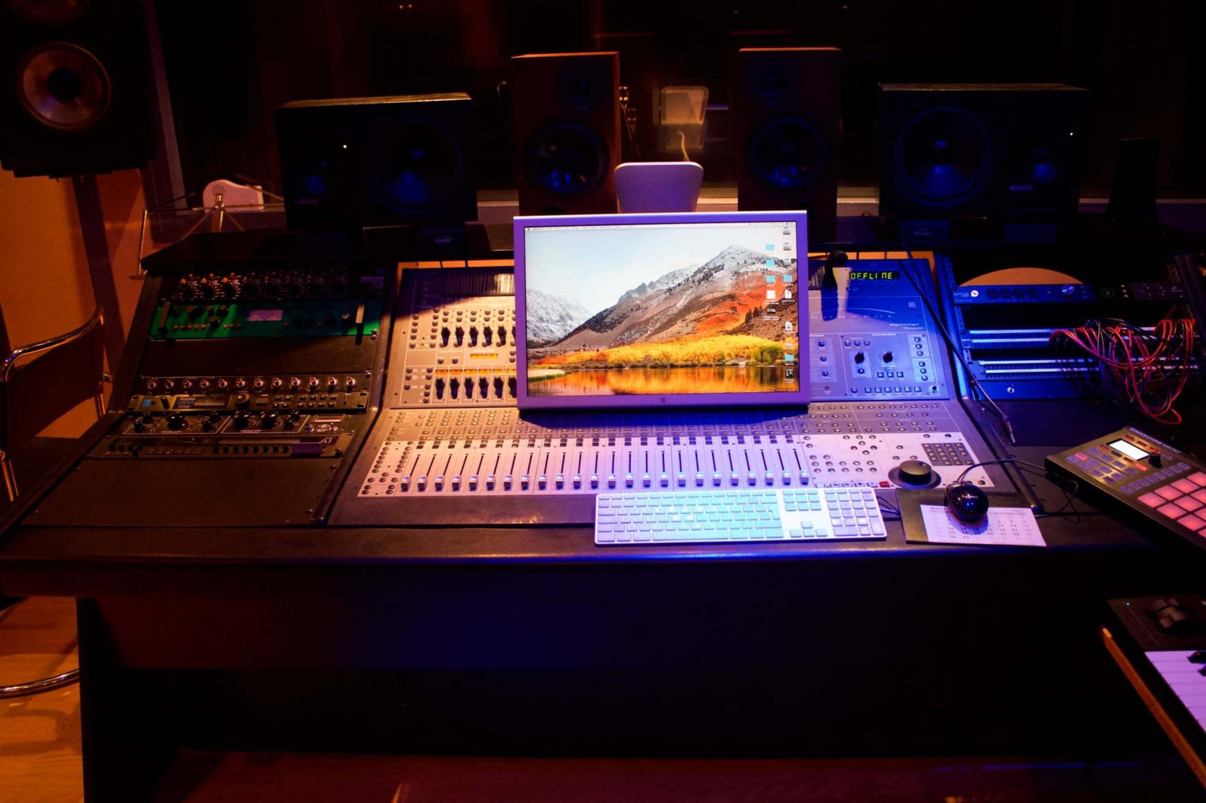 A recording studio control panel equipped with audio equipment, a computer, and monitors.