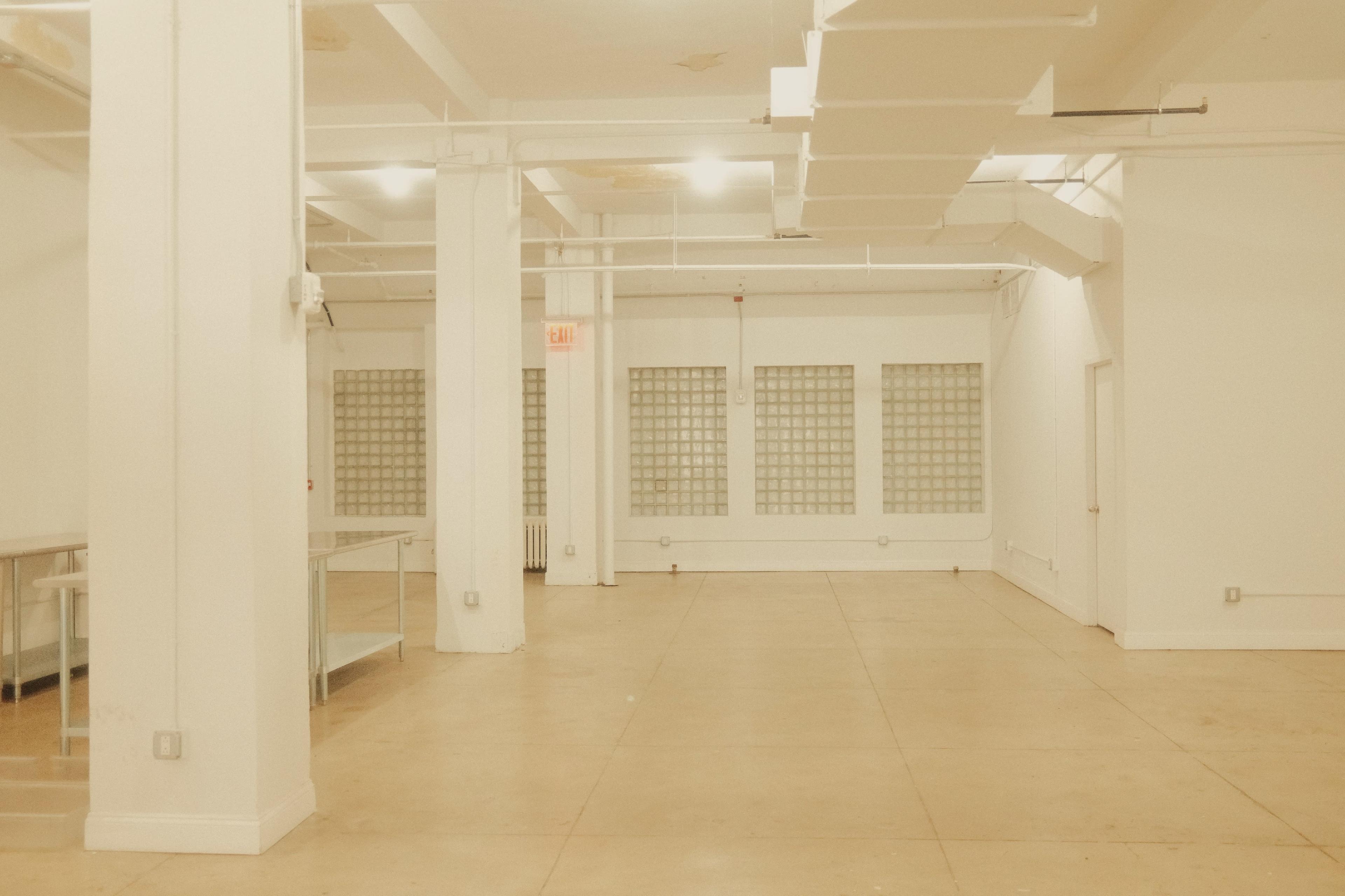 The image shows an empty, well-lit interior space with concrete floors and white walls, featuring glass block windows along one side.