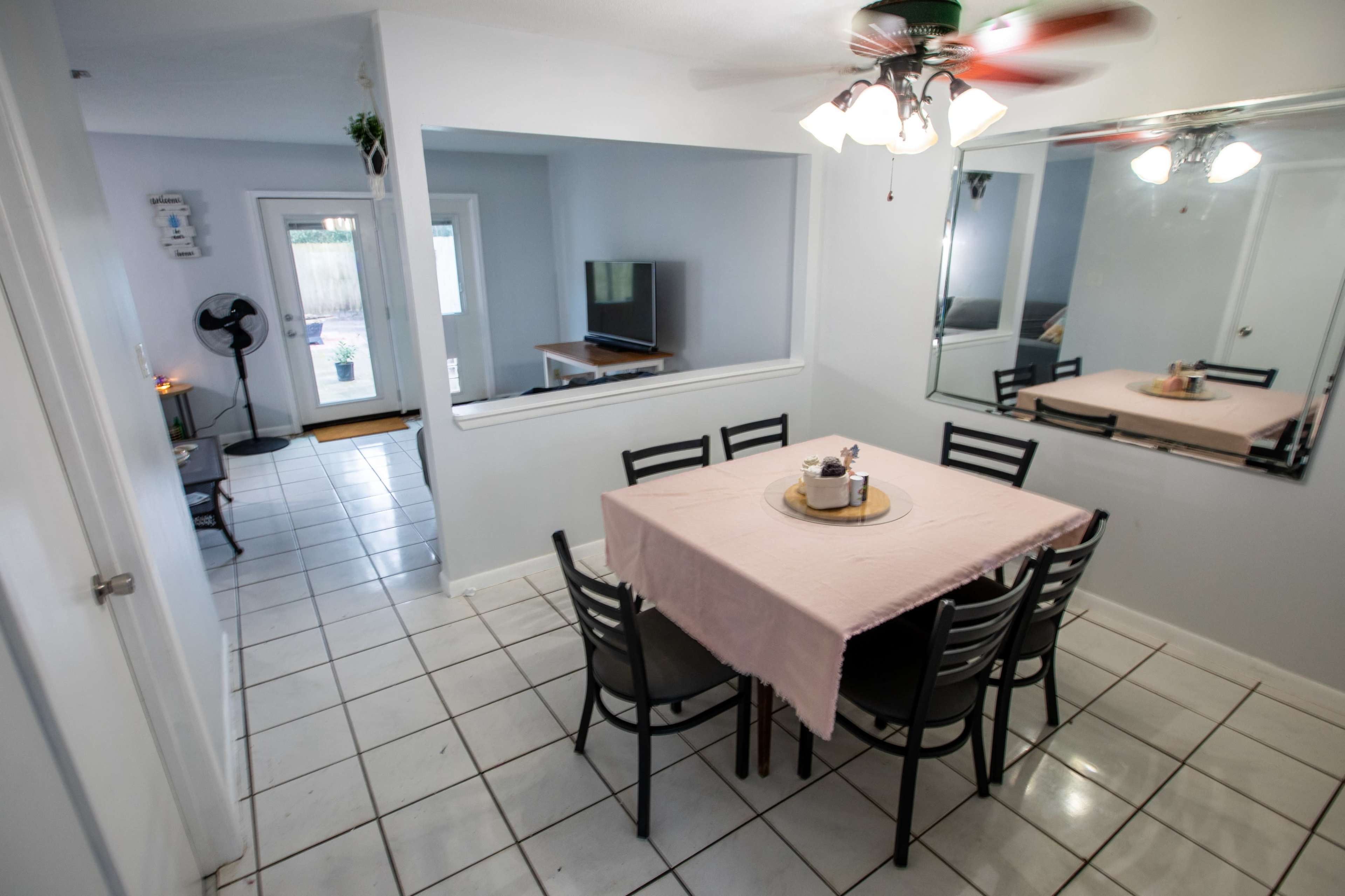 A dining area features a rectangular table with six black chairs, surrounded by light-colored walls and tiled flooring.