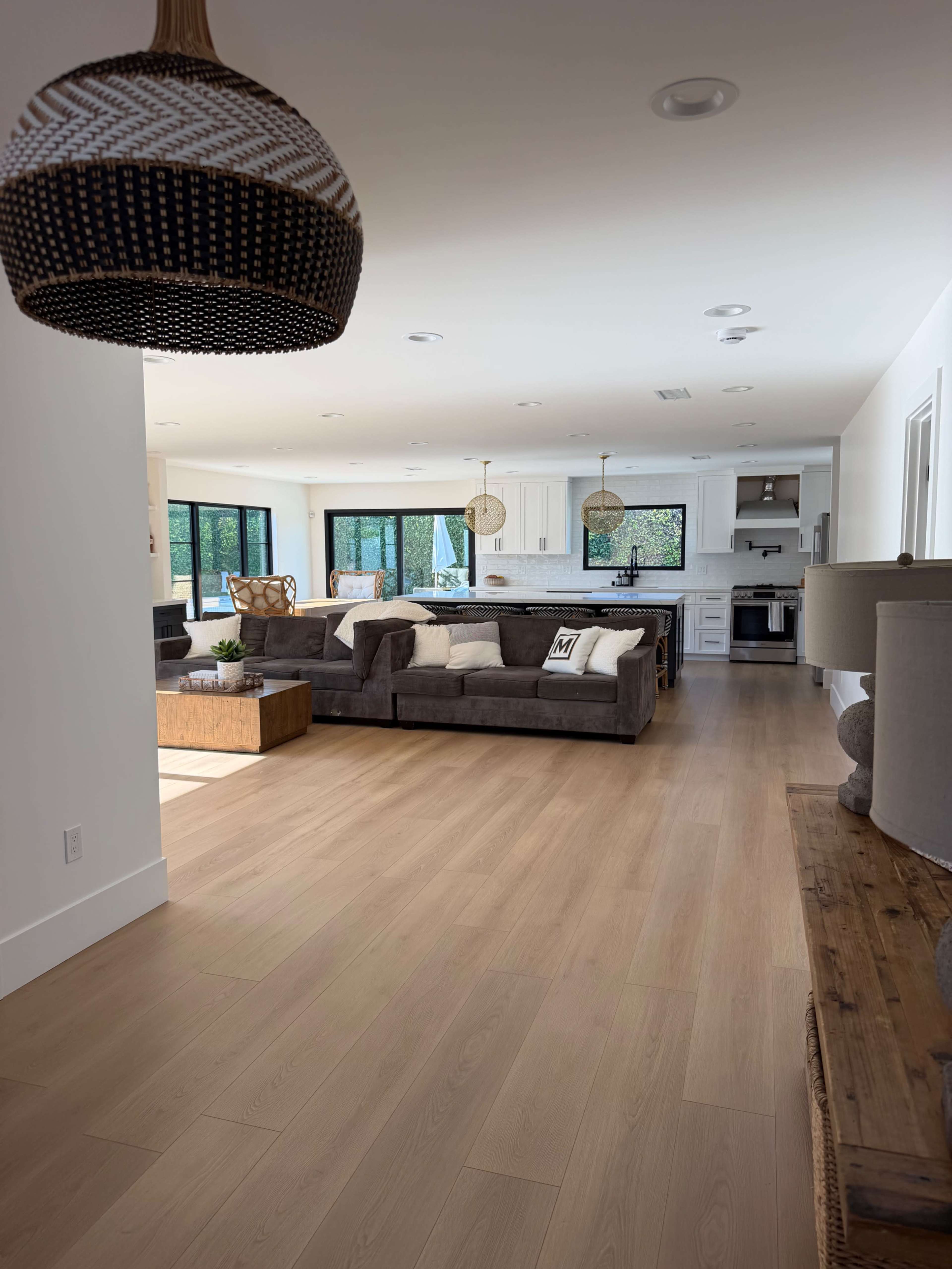 The image shows a spacious, modern living area with a large sectional sofa, a coffee table, and a kitchen visible in the background.