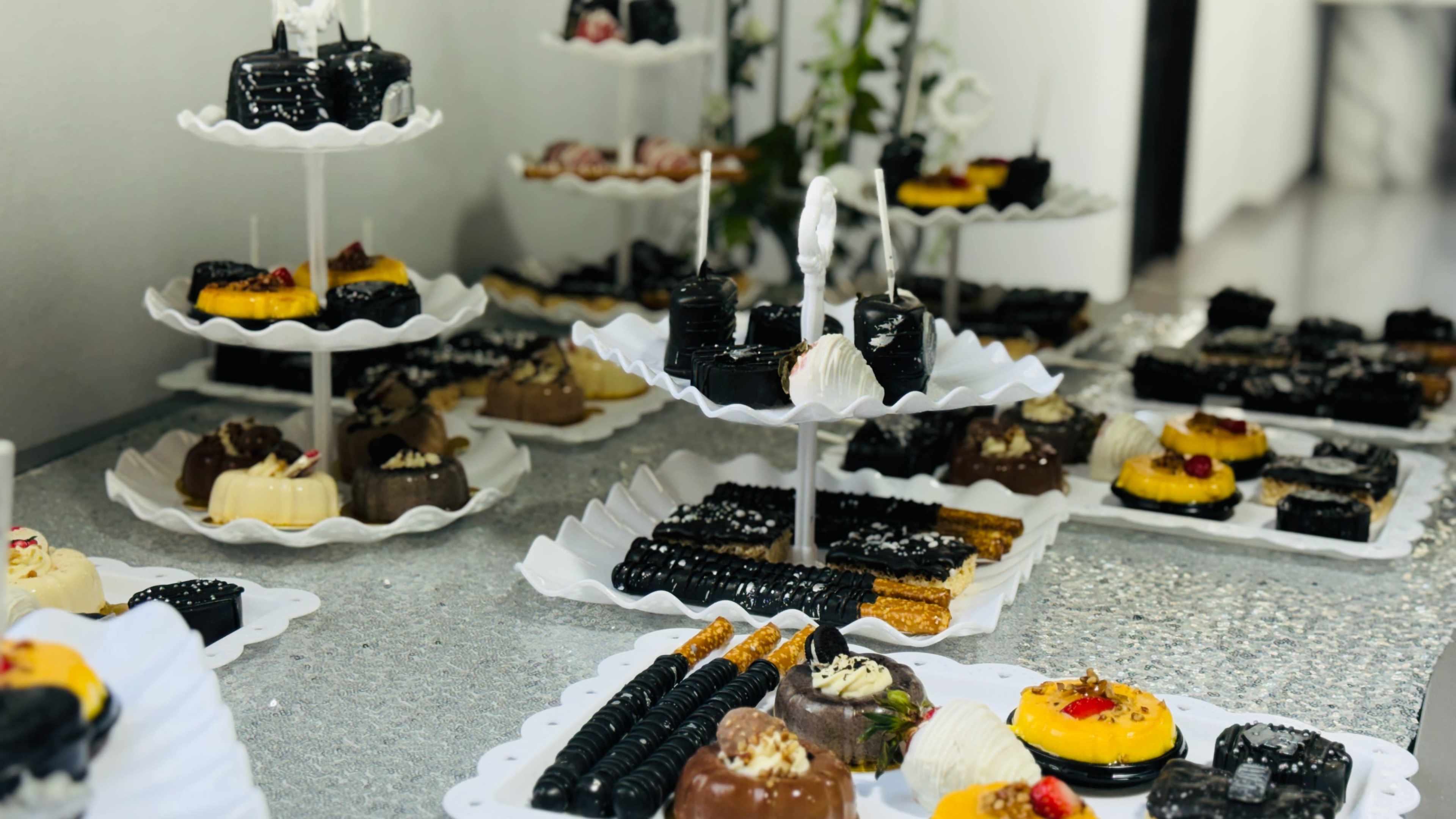 The image showcases an assortment of desserts arranged on tiered serving plates, featuring various chocolates, cakes, and pastries.
