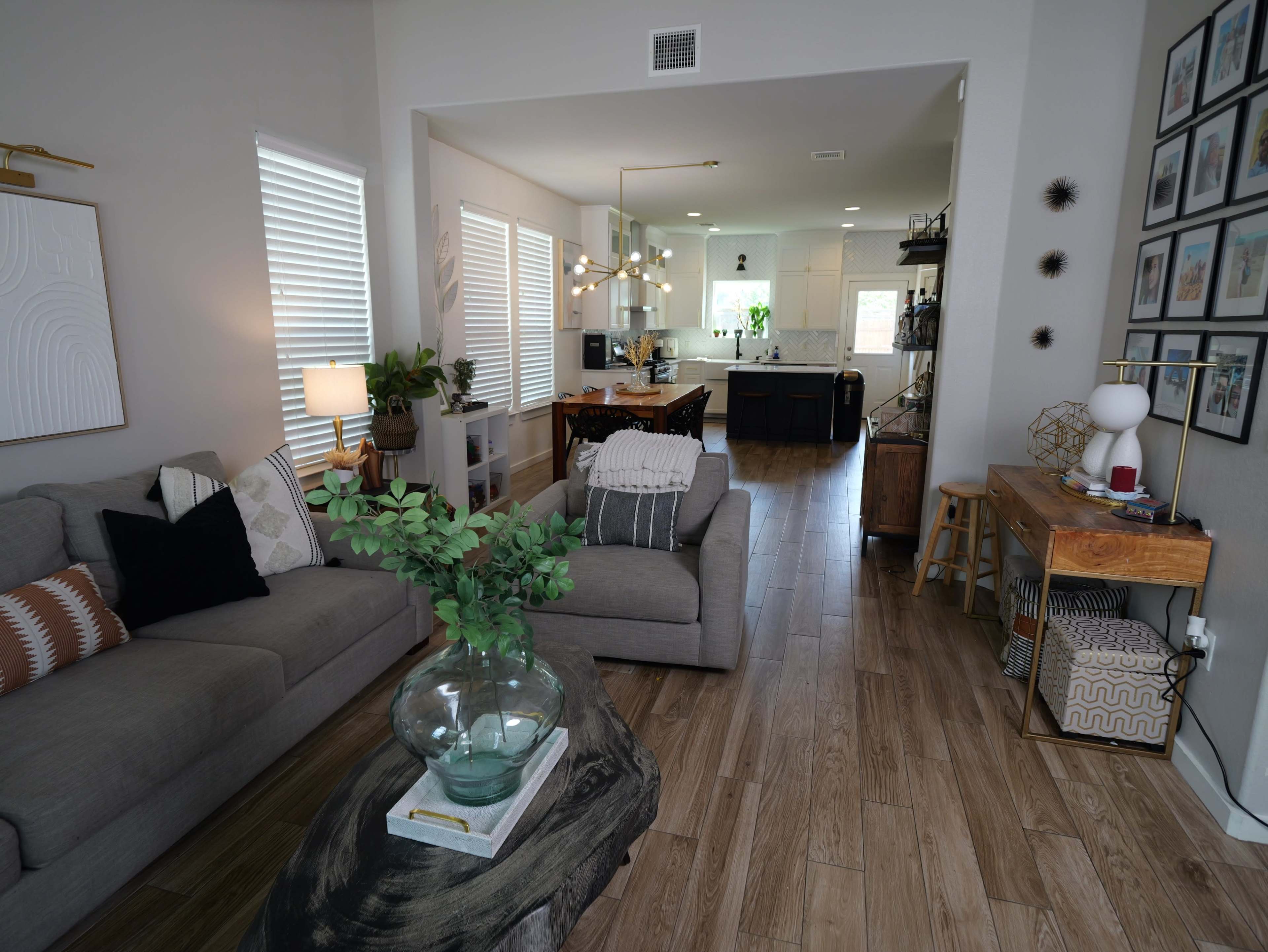 A spacious living room features a gray sofa, a wooden coffee table, and a view into a modern kitchen with black cabinetry.
