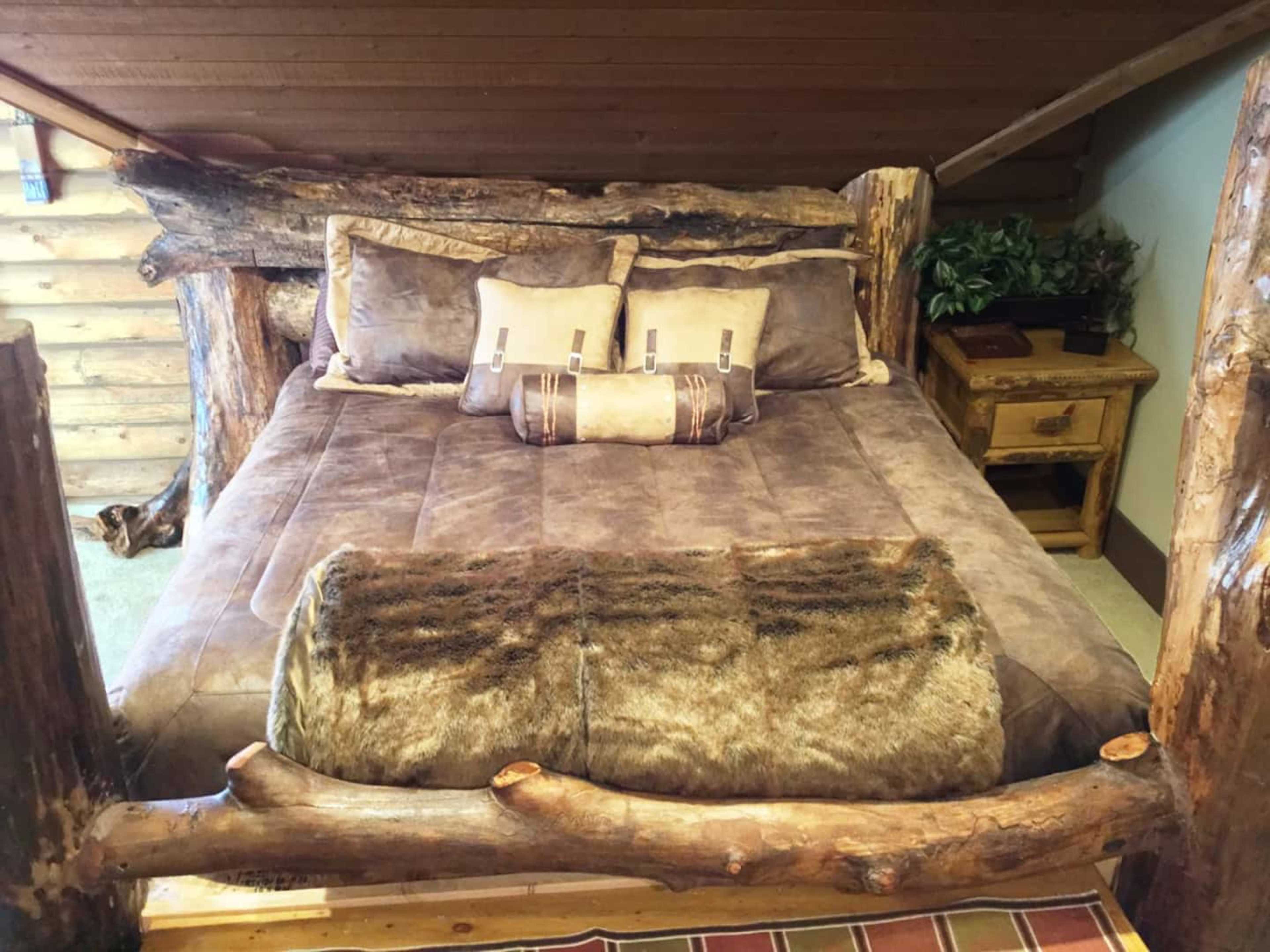 A rustic wooden bed with a log frame and gray bedding is positioned in a cabin-like room.