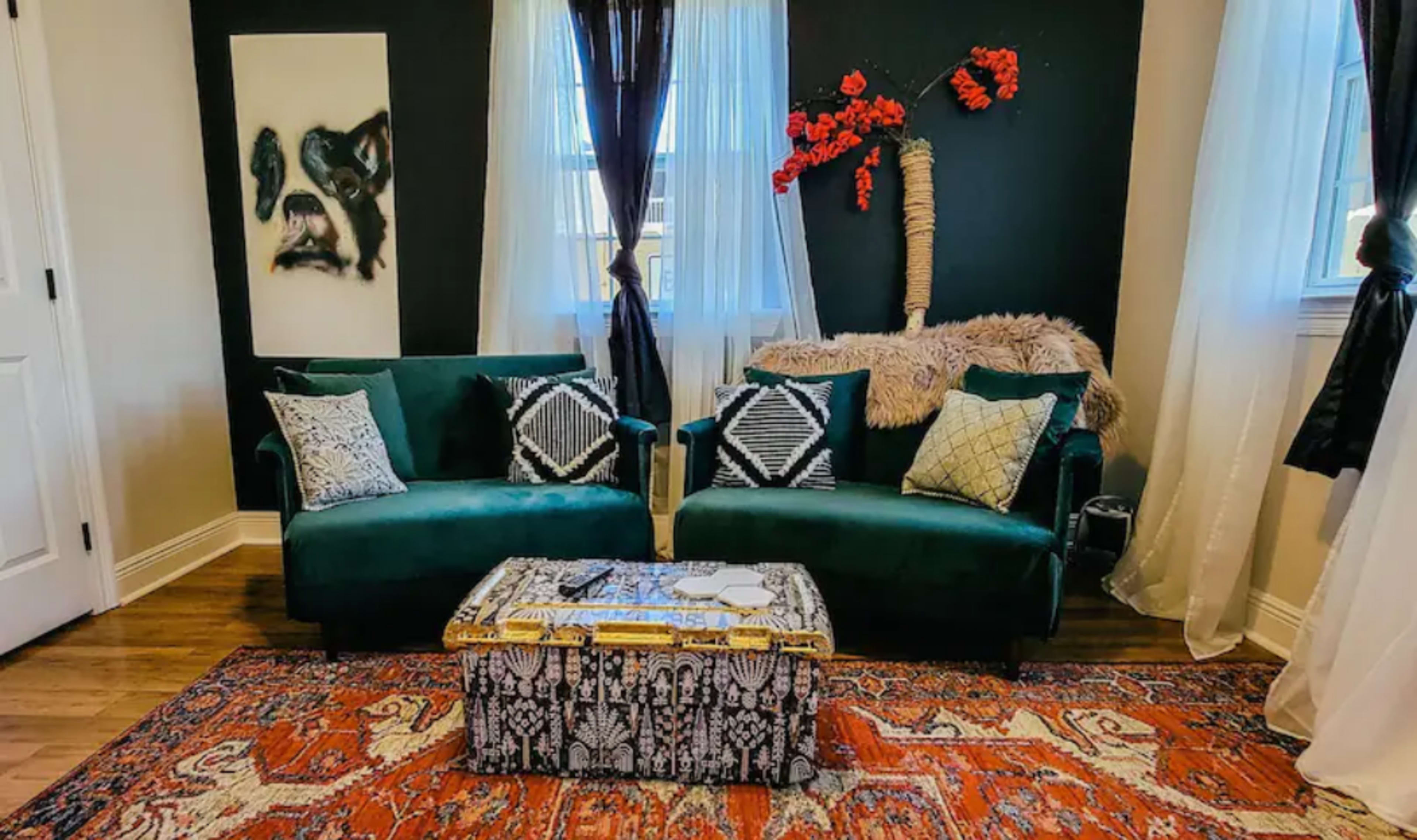 A stylish living room featuring two green velvet sofas, a patterned area rug, and decorative wall art.