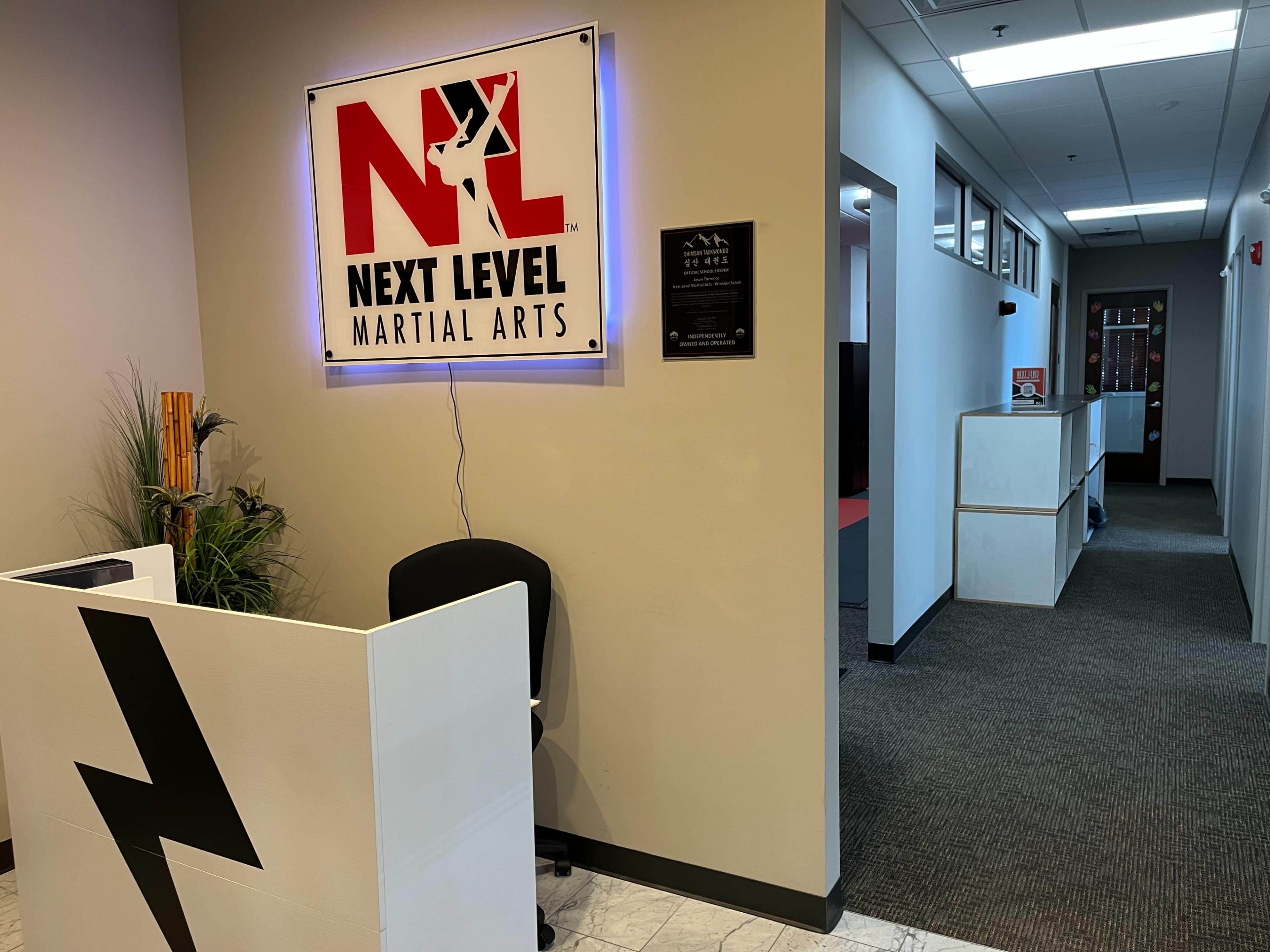 The image shows the interior of a martial arts studio, featuring a reception area with a desk and a sign that says "Next Level Martial Arts" on the wall.