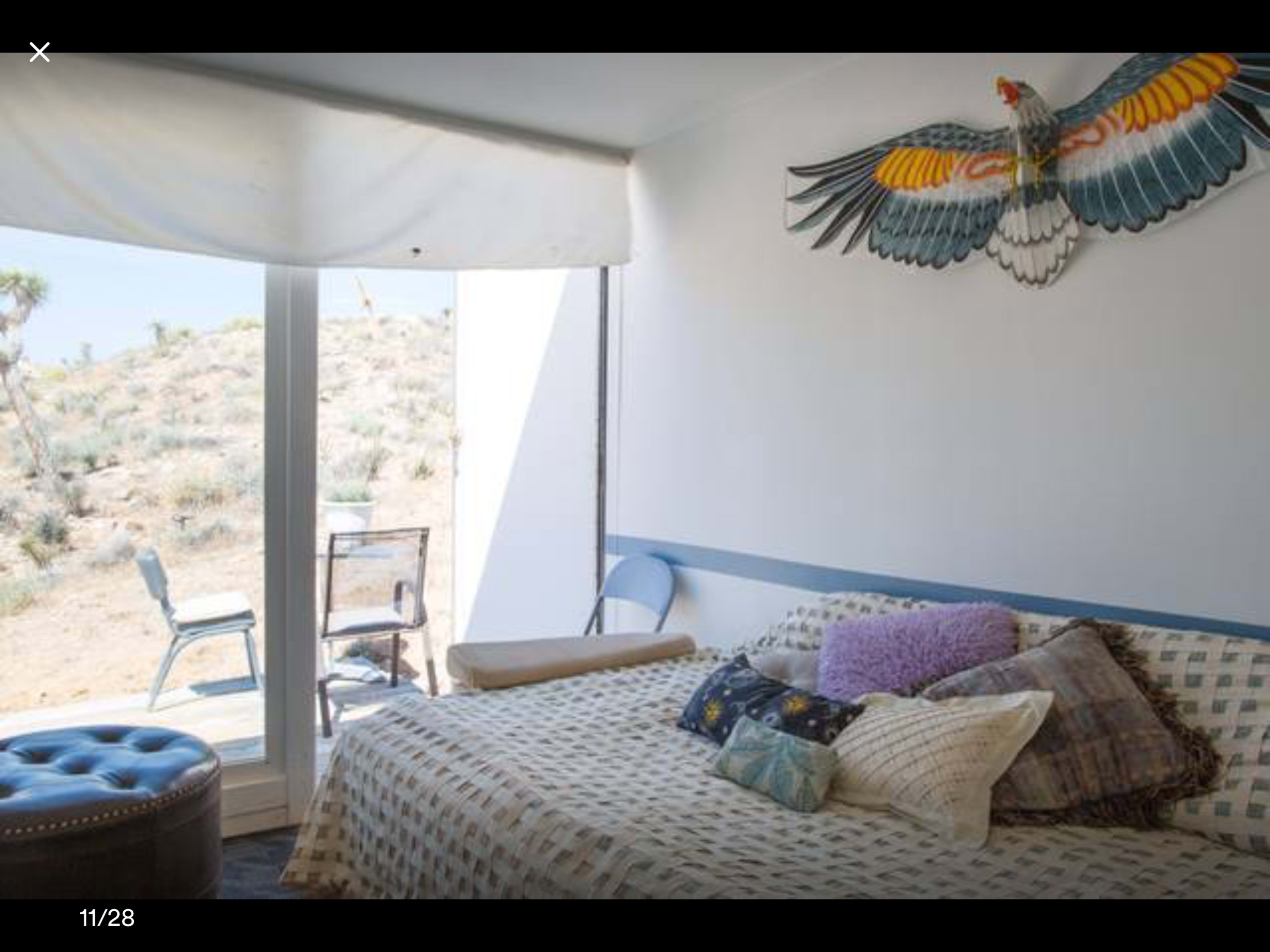 The room features a bed with various pillows and a large bird decoration on the wall, with a view of a desert landscape through sliding glass doors.