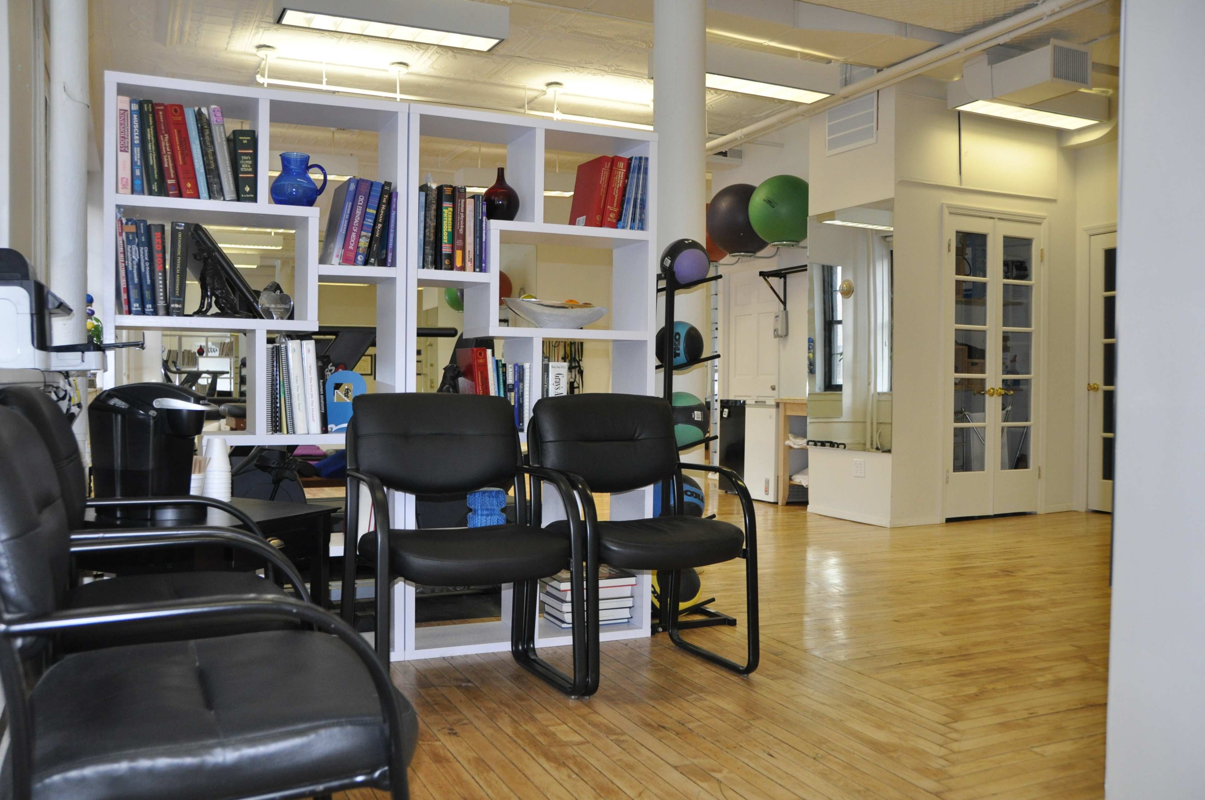 A spacious room with black chairs, a bookshelf filled with books, and exercise equipment in the background.