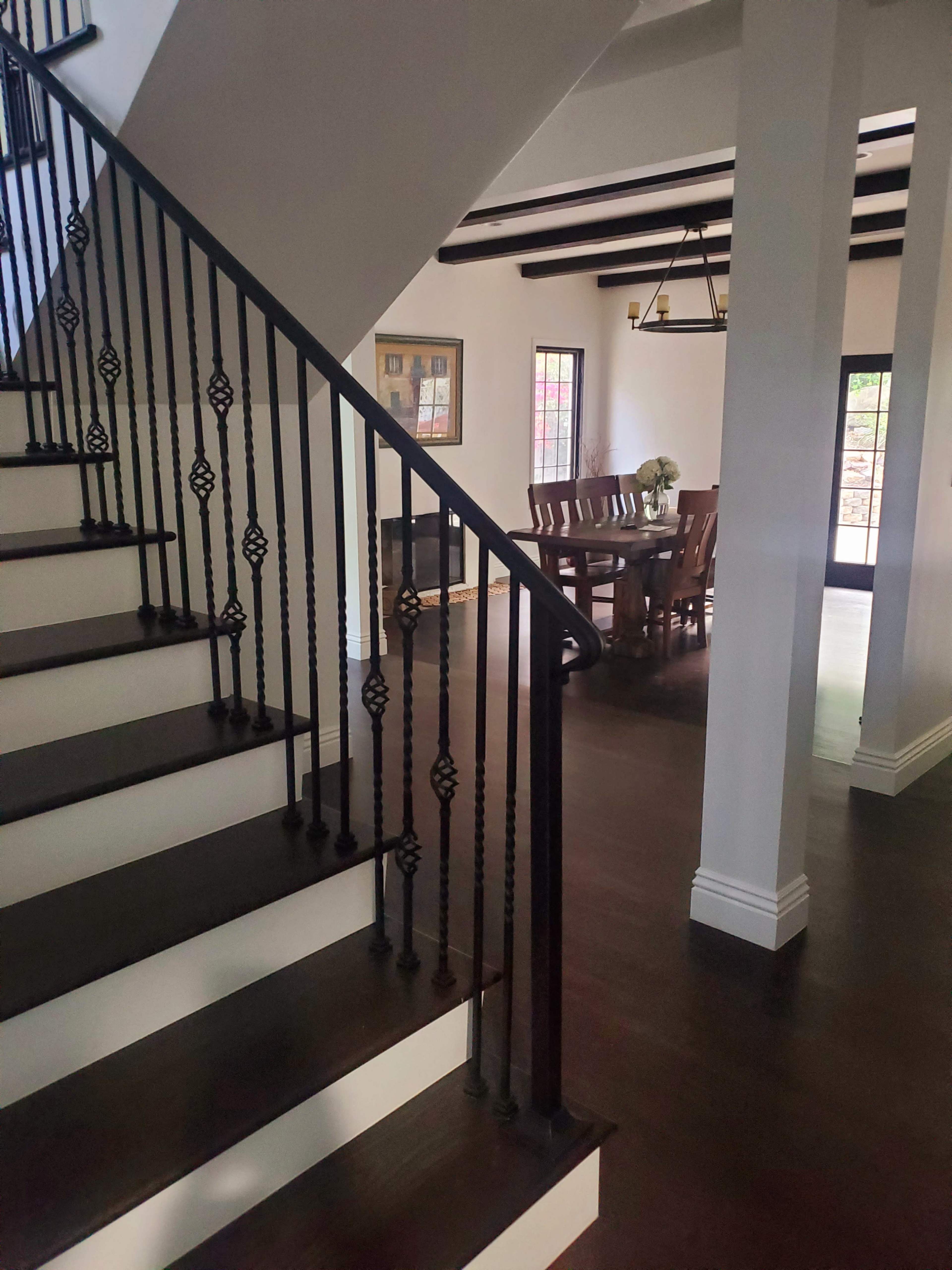 The image shows a staircase with black wrought iron railing leading to a dining area with a long wooden table and chairs.