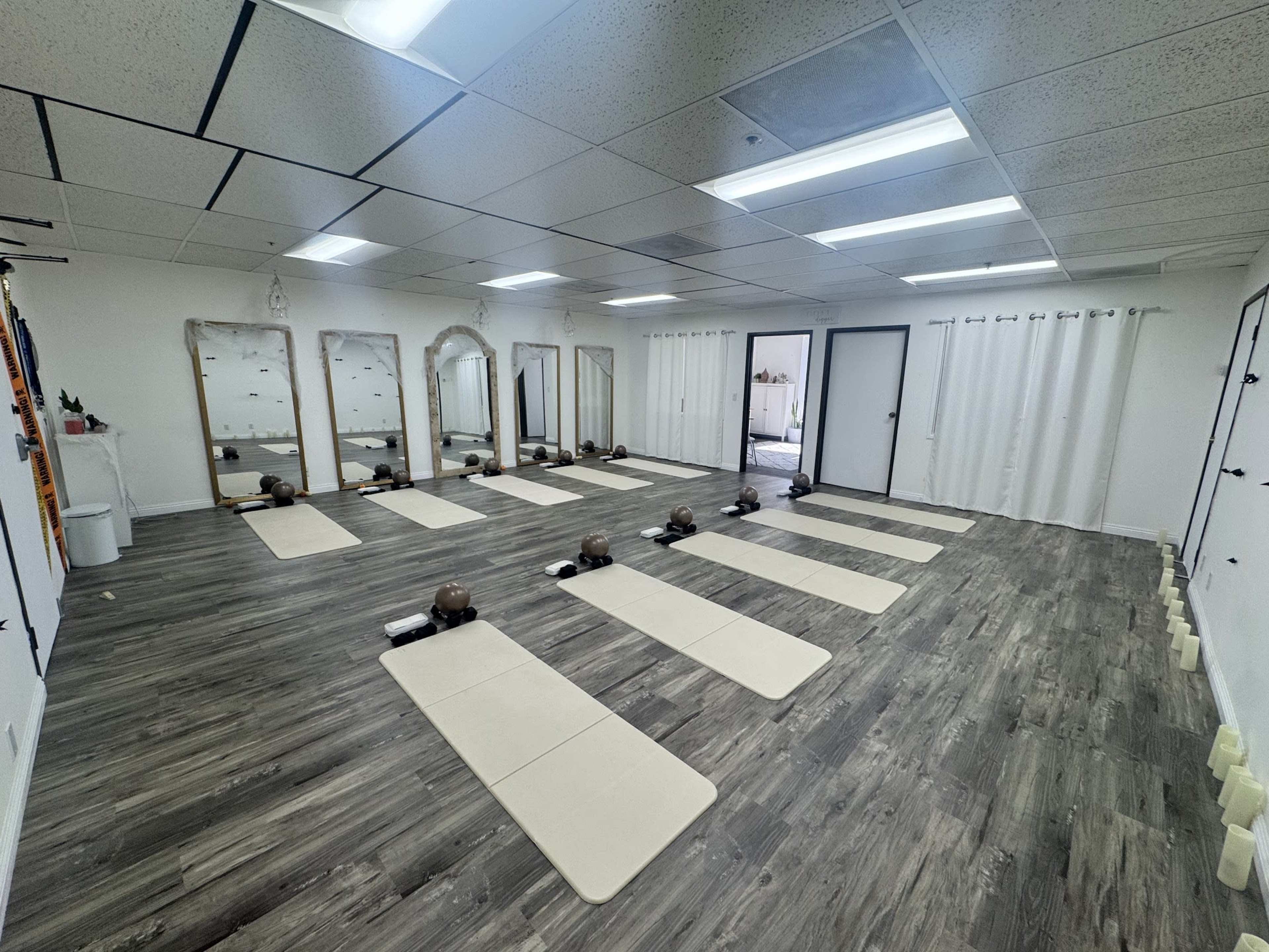 The image shows a spacious yoga studio with several exercise mats arranged neatly on the floor, surrounded by mirrors and natural lighting.