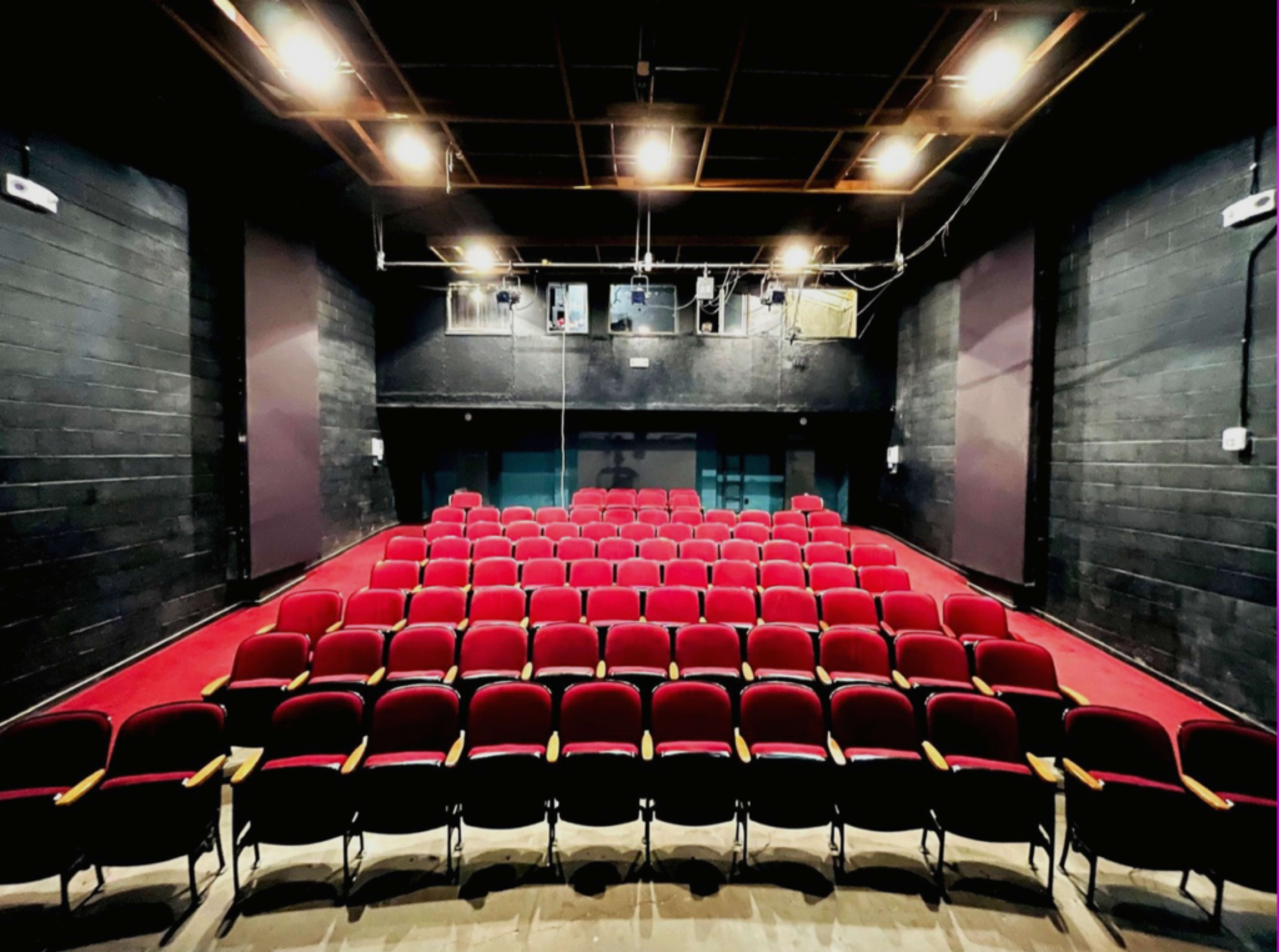 A theater with rows of red seats arranged in front of a dark stage and black walls.